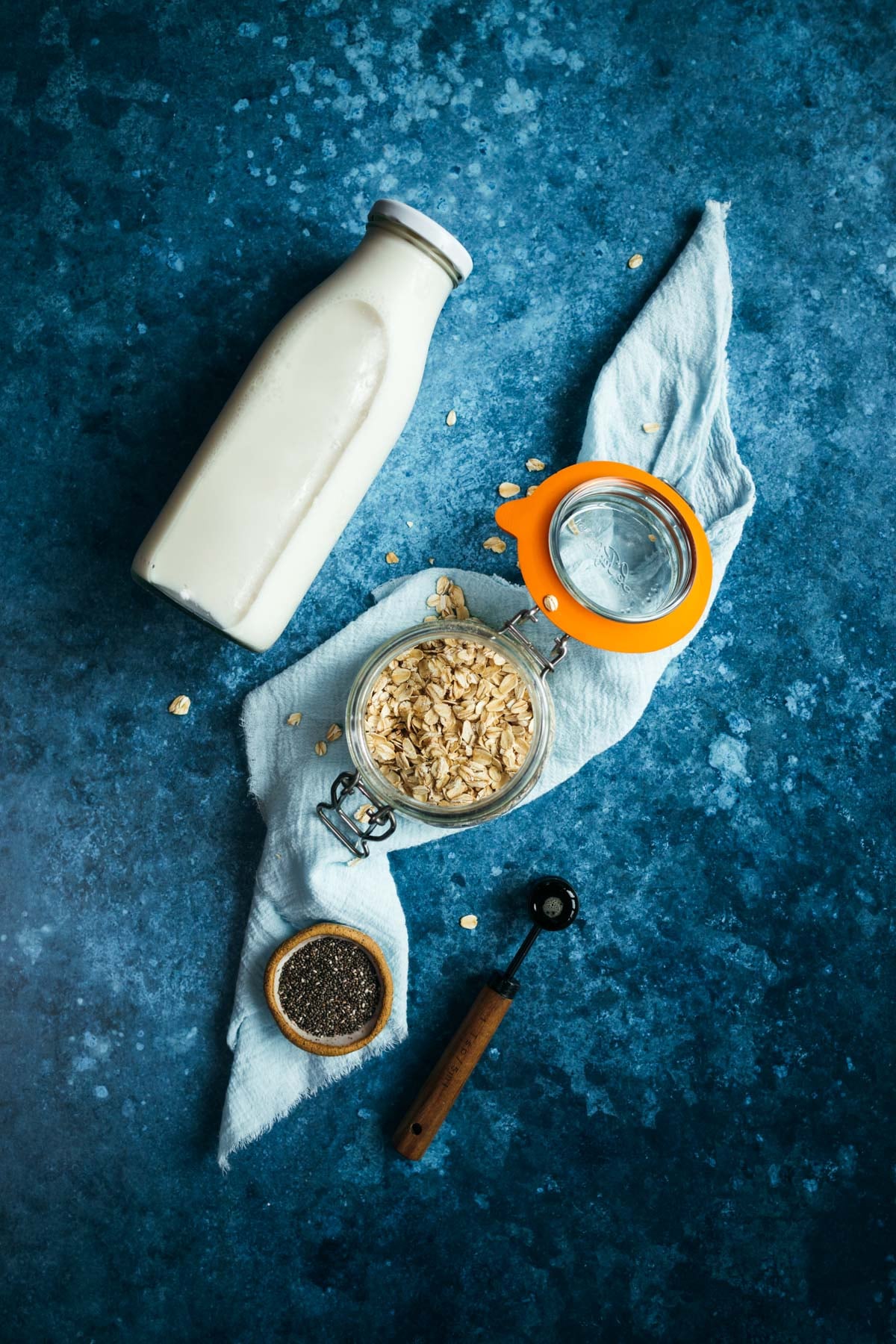 A bottle of milk, oats and a spoon on a blue background.