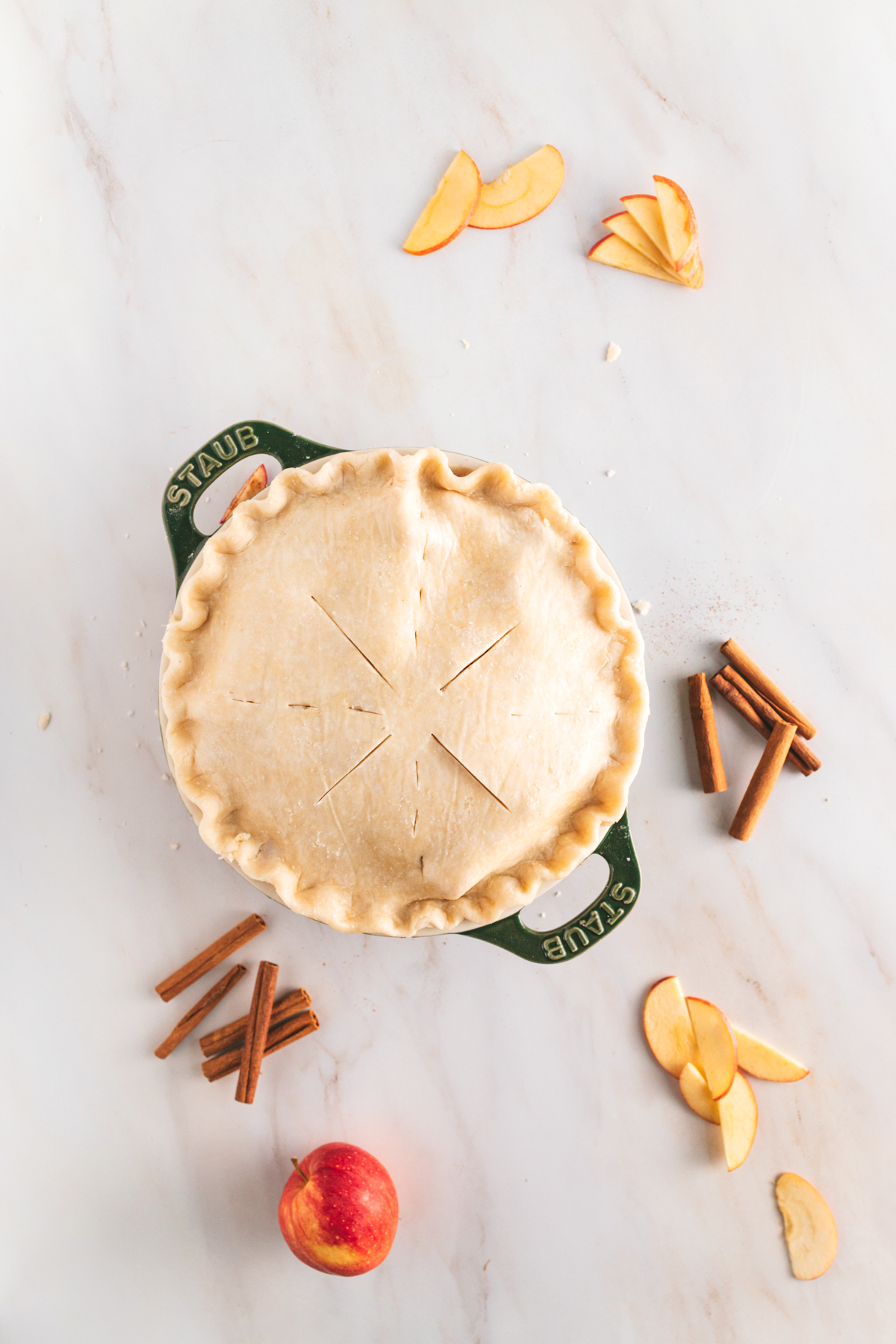 A pie with apples and cinnamon on a marble countertop.