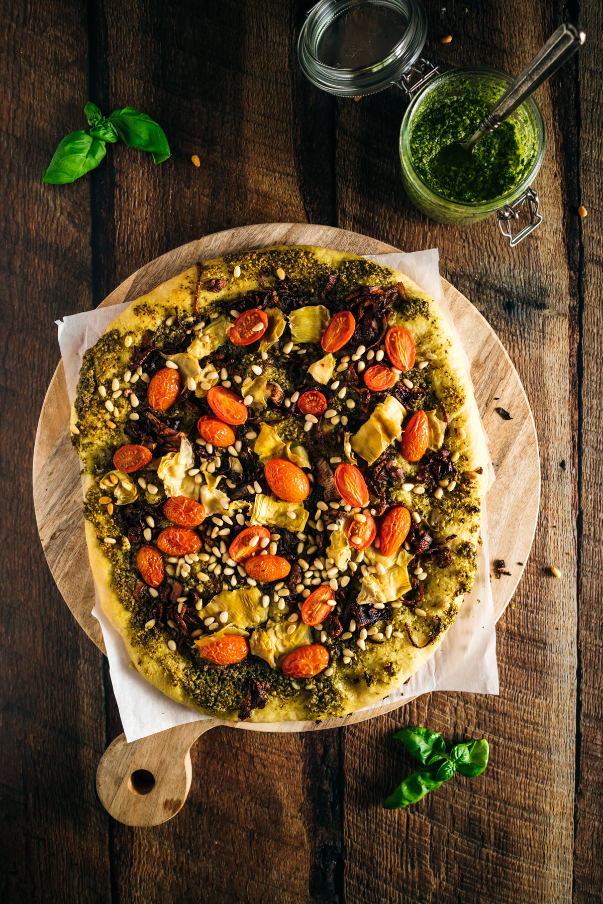 A cooked pizza with pesto and tomatoes on a wooden board.