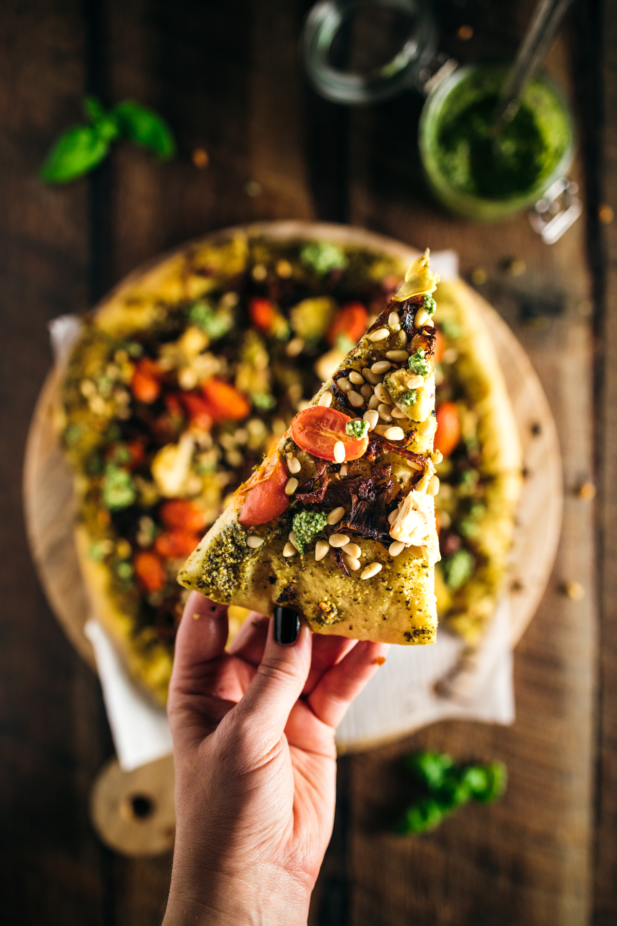 A hand holding a slice of pizza on a wooden board.