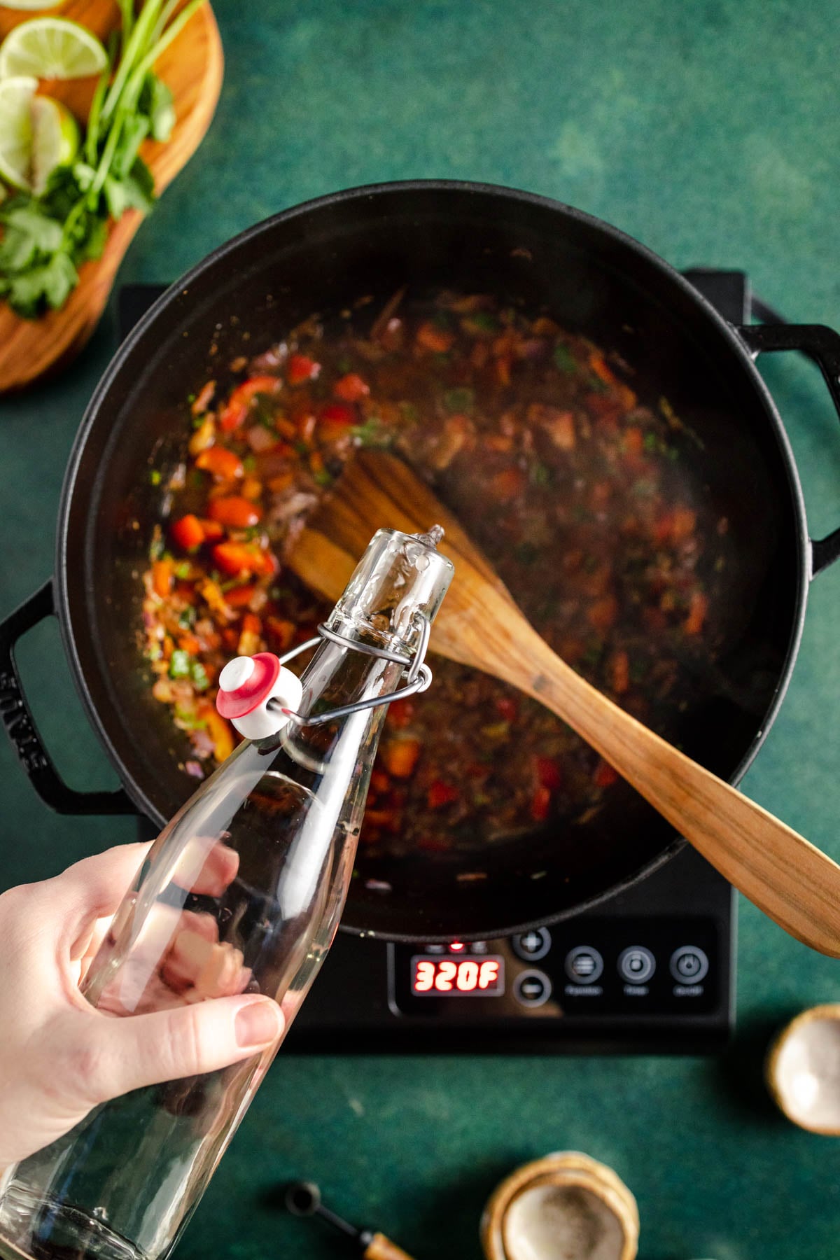 A person pouring a glass water into a pot of food.