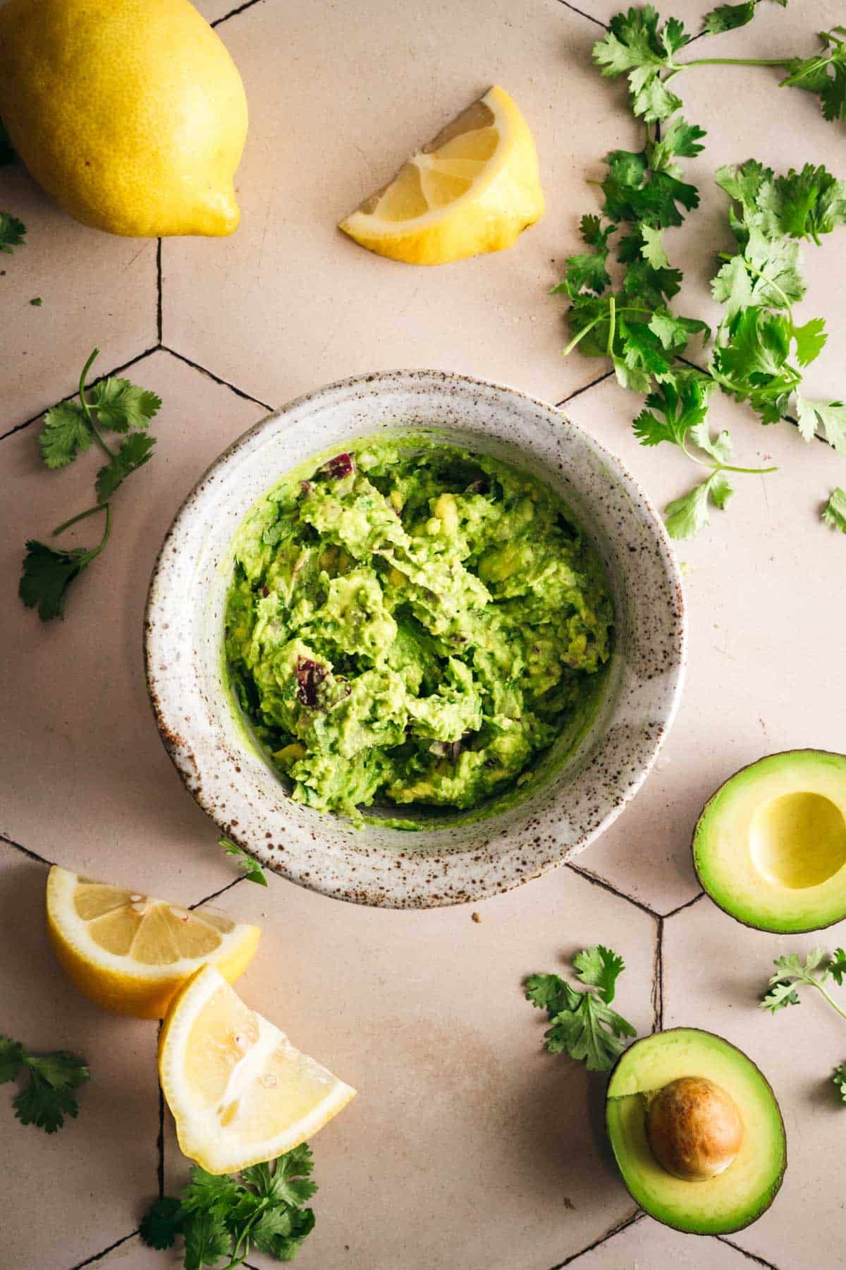 Fresh homemade guacamole with avocado, lemon and herbs on a tile counter.