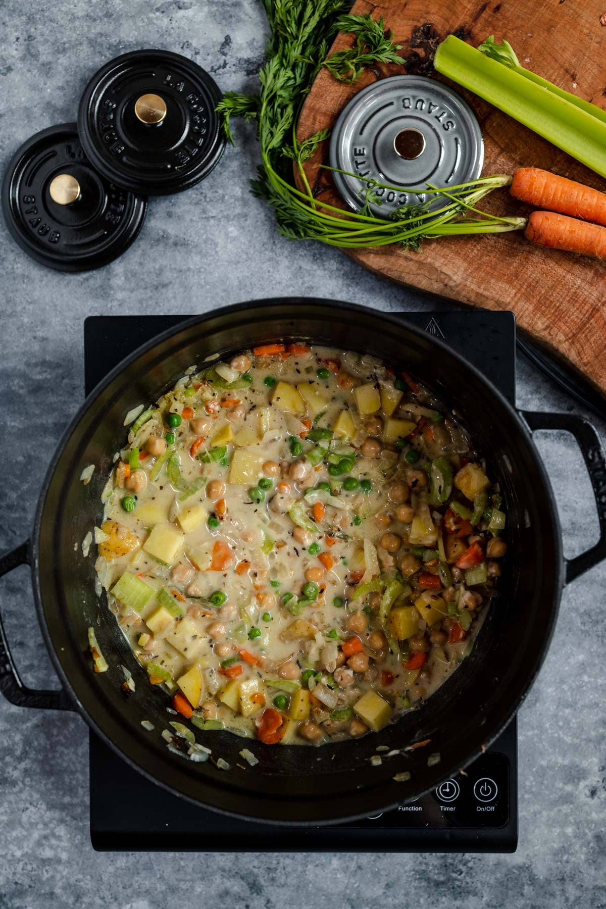 A pot of vegetable soup cooking on a stovetop, surrounded by fresh ingredients and a ladle.