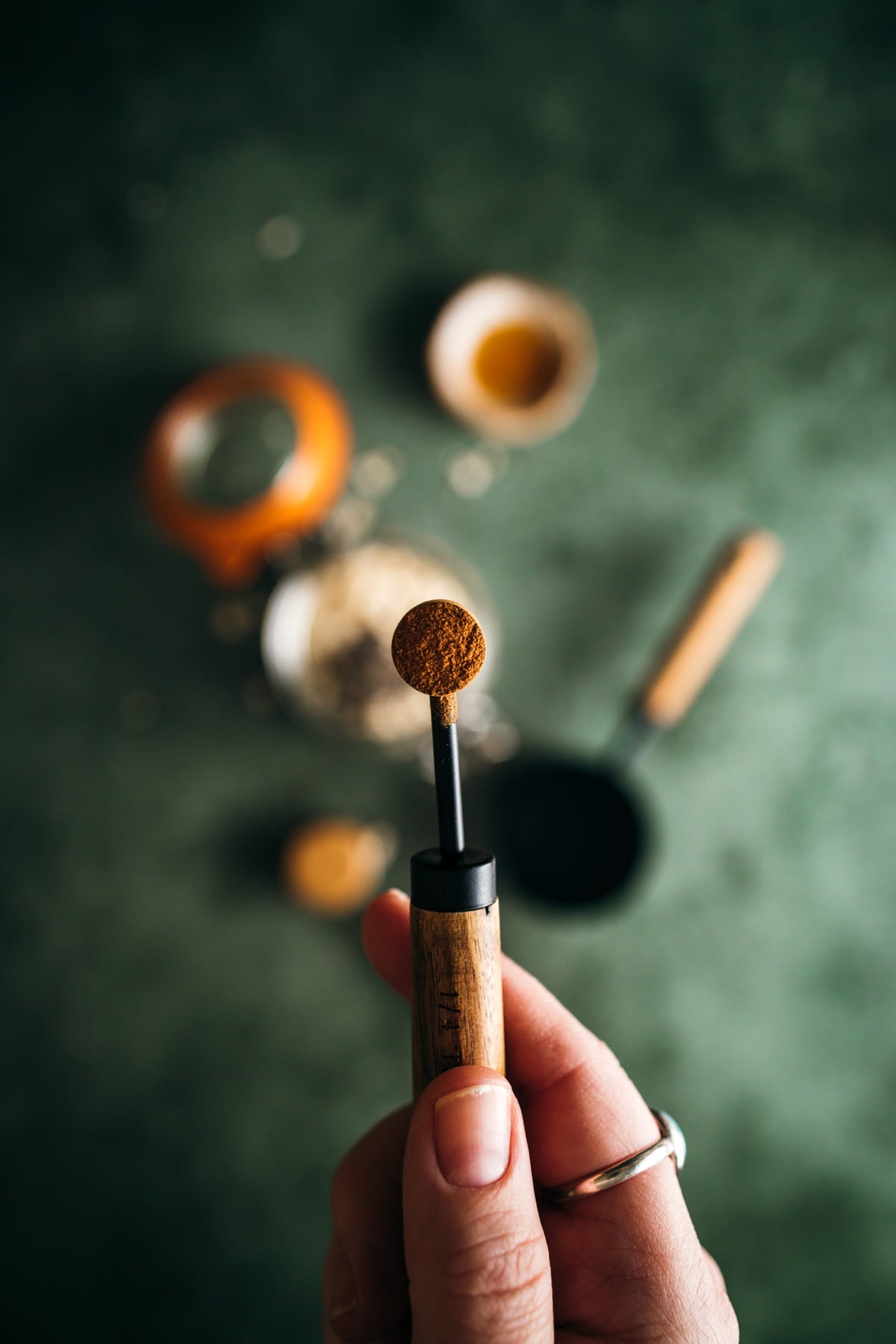 A person holding a measuring spoon with ground coffee over a coffee maker setup.