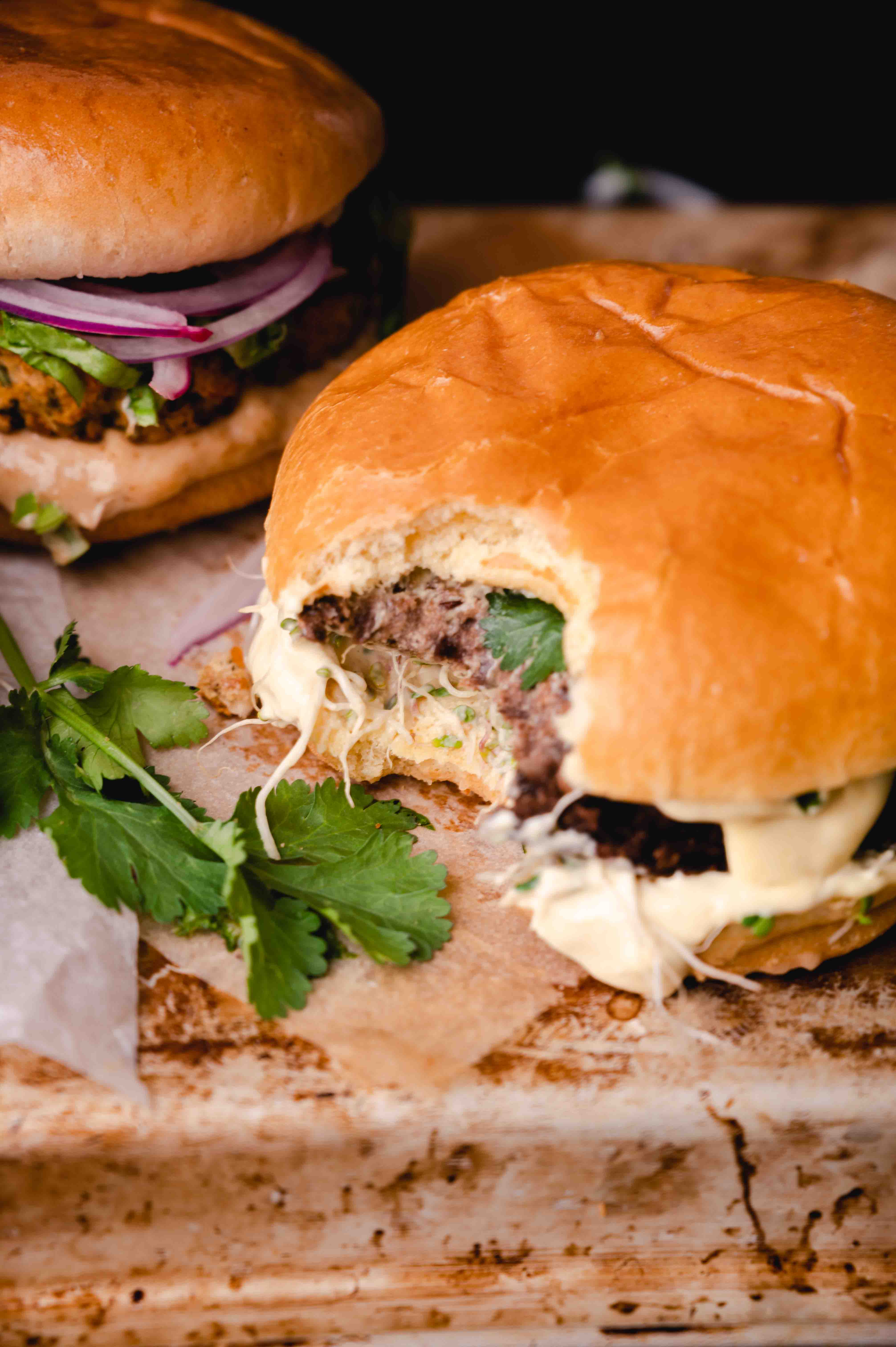 Two burgers with buns, one with a visible bean patty and fresh toppings, presented on a rustic wooden surface.