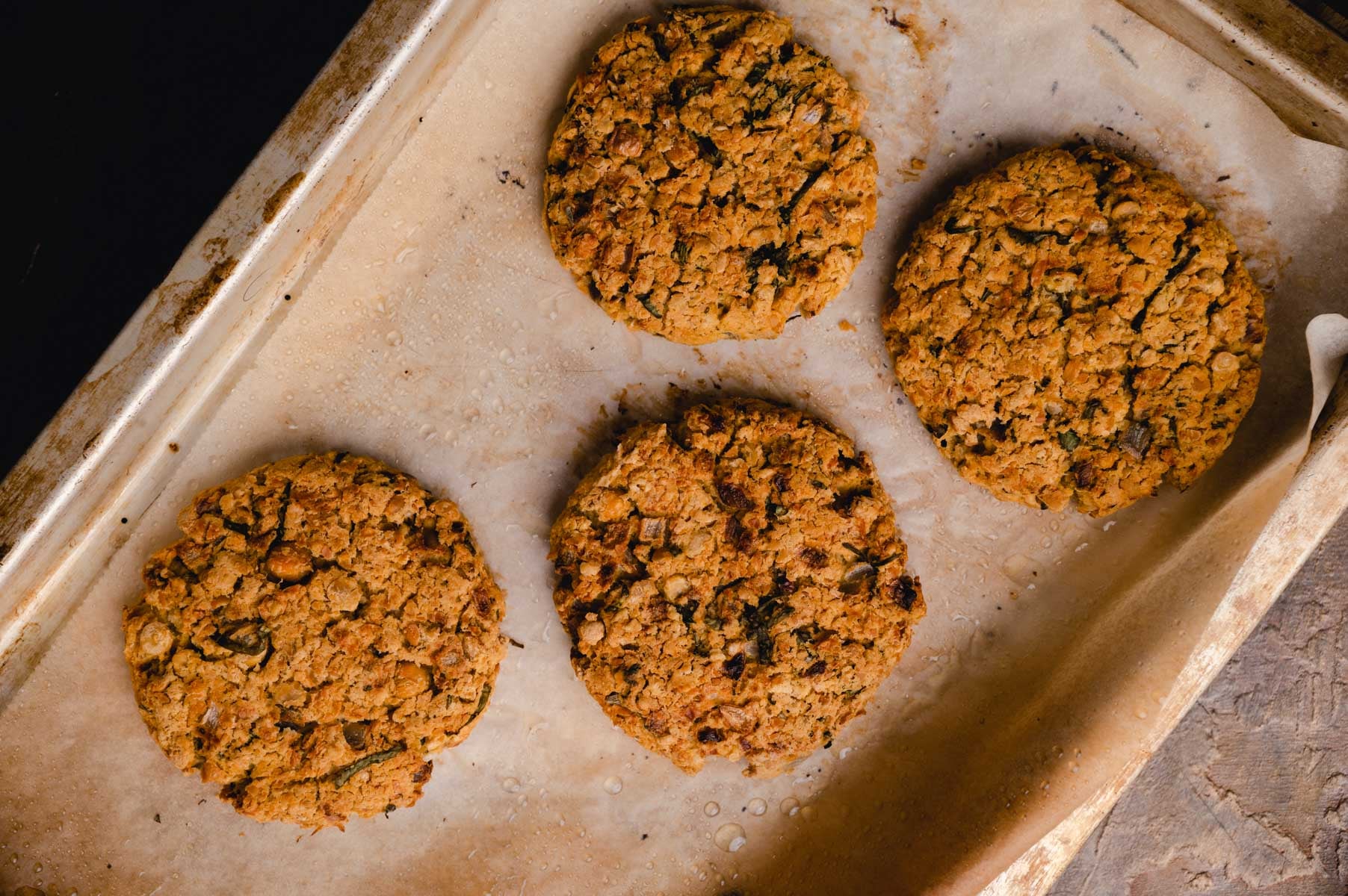 Four freshly baked oatmeal raisin cookies on parchment paper on a baking tray.