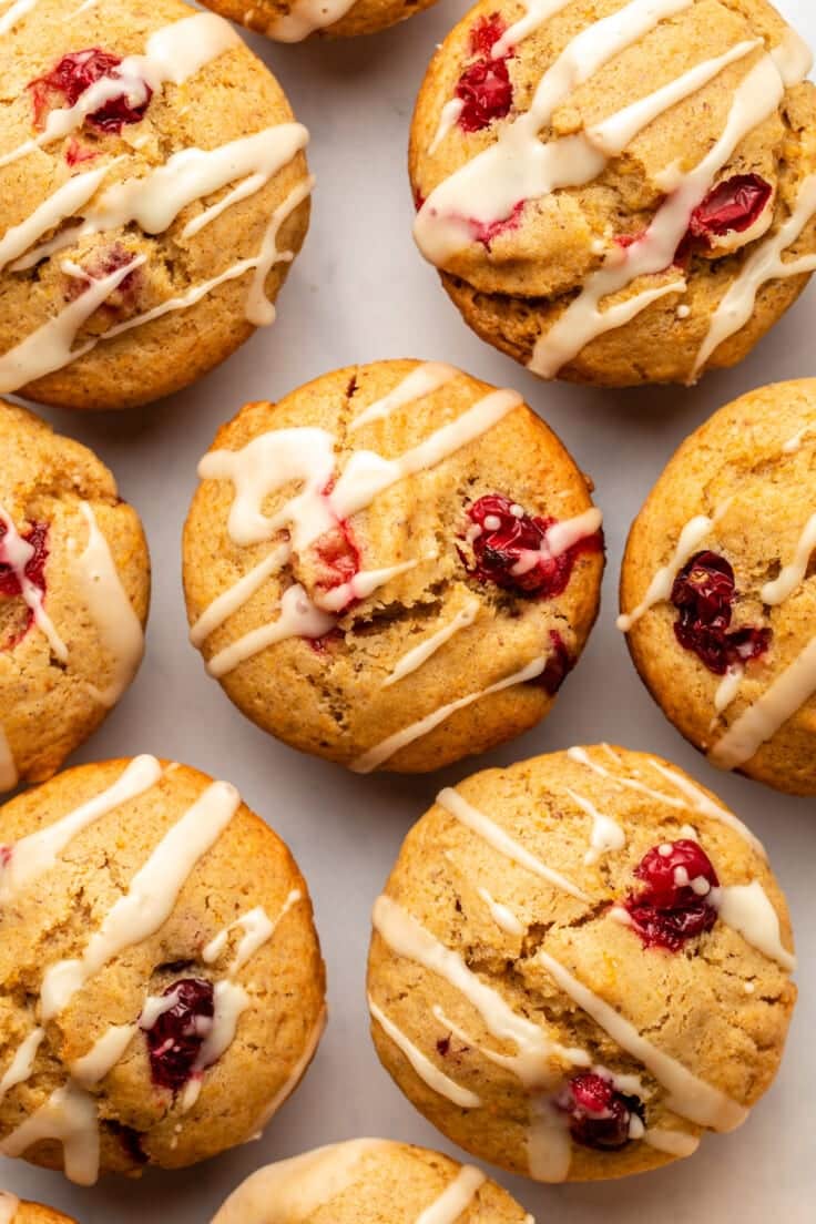 Close-up of freshly baked vegan cranberry muffins topped with white glaze on a light background.
