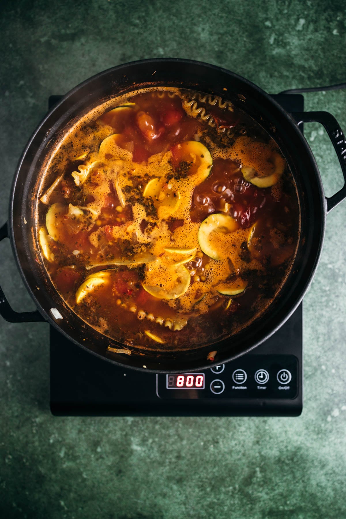 Soup with tomatoes and pasta simmering in an electric pressure cooker on a kitchen counter.