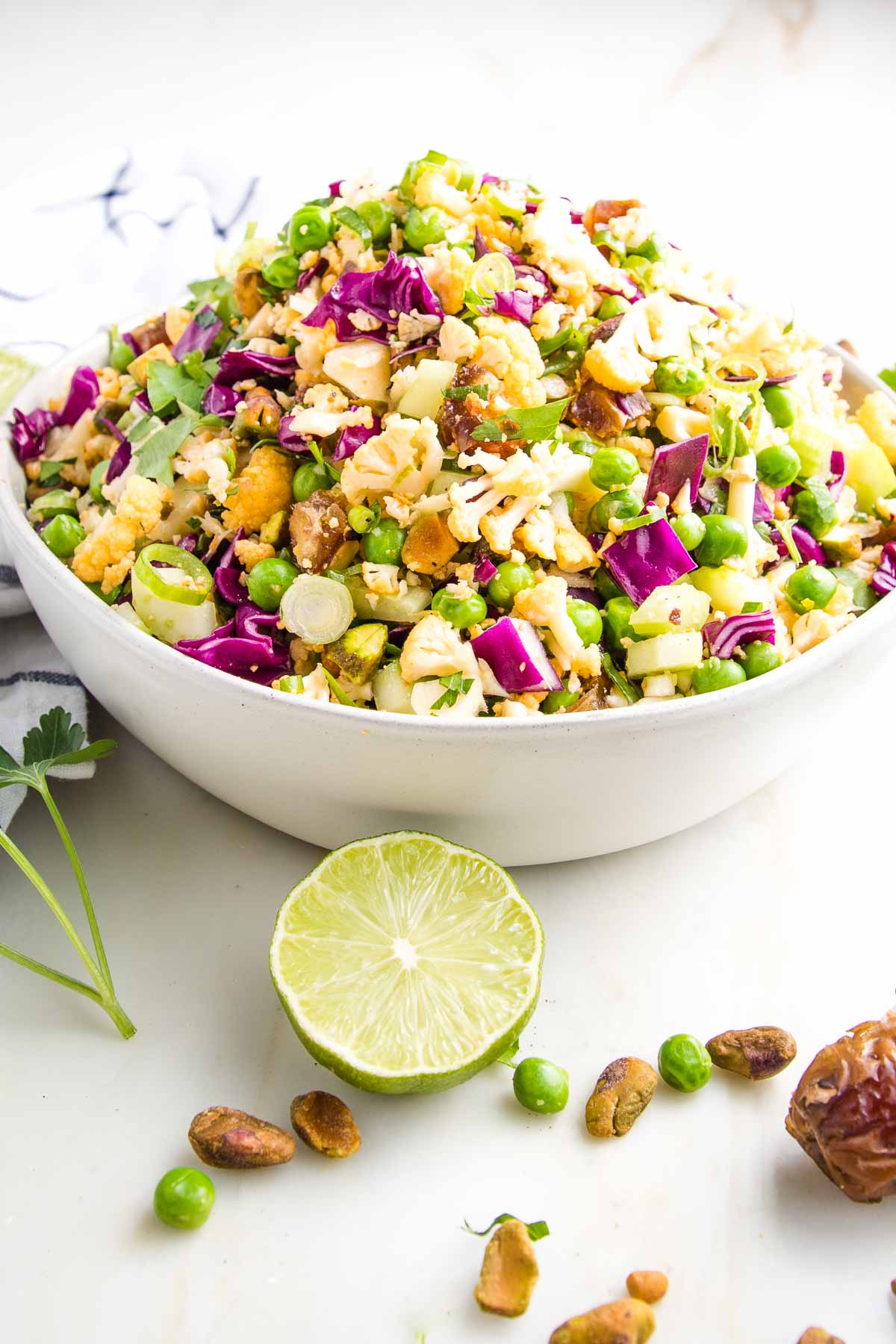 A colorful bowl of chopped salad with red cabbage, green apples, pistachios, and crumbled cheese, garnished with a lime wedge and parsley. This tasty dish can serve as the perfect accom