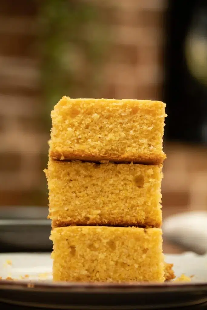 Three stacked slices of moist cornbread on a plate, set against a softly blurred background, perfect as tasty side dishes.