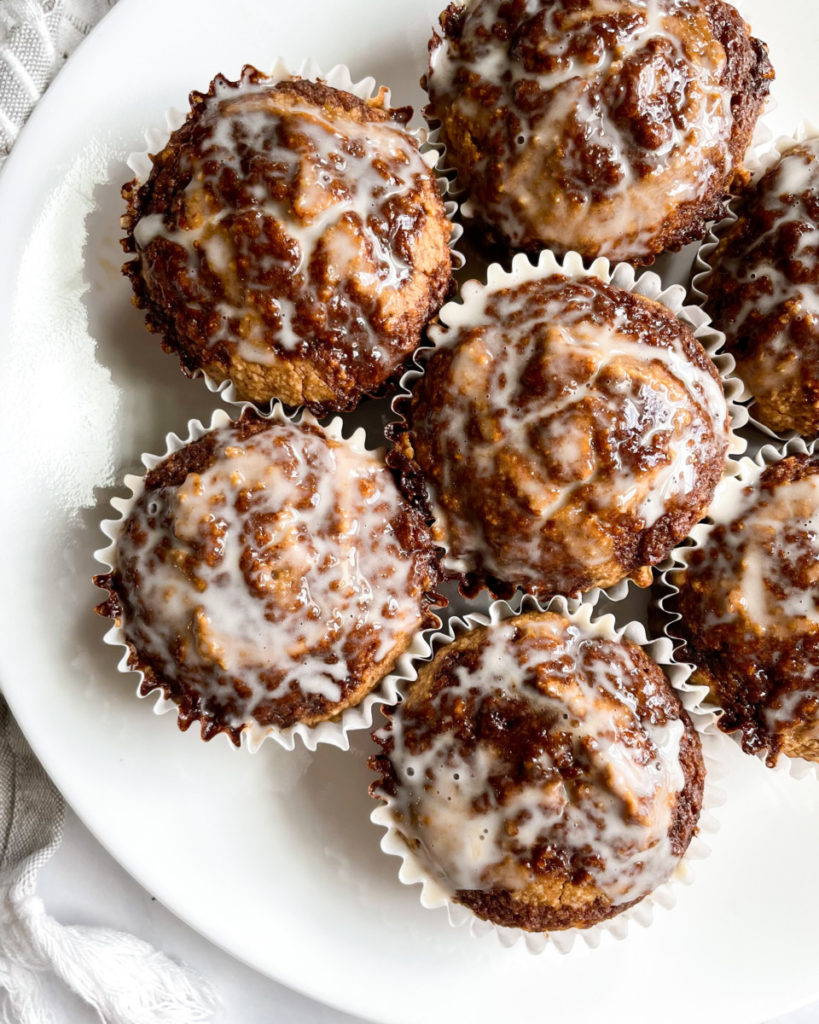 A plate of freshly baked vegan muffins with a glazed topping, served in white paper liners.
