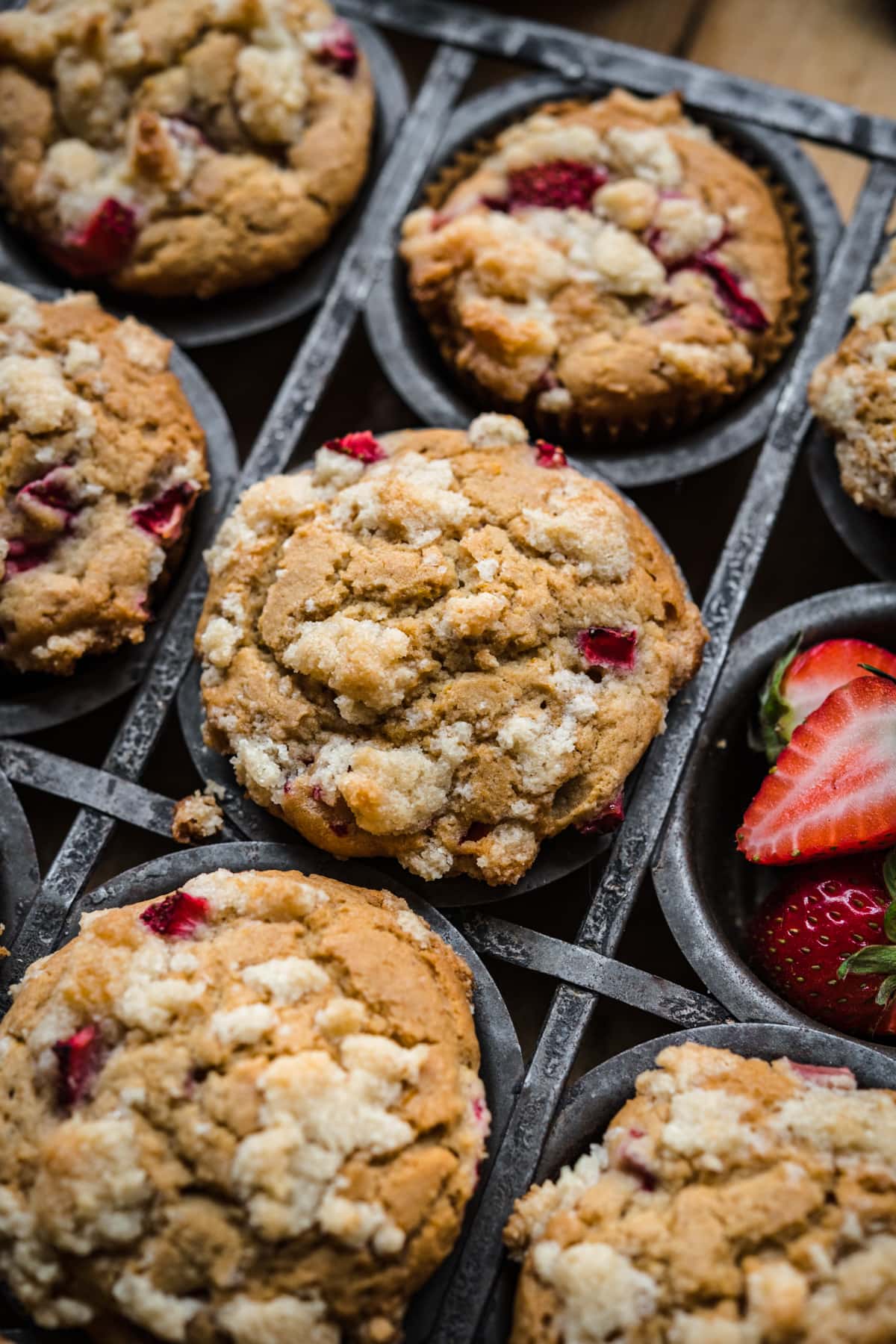 Freshly baked vegan strawberry muffins in a dark metal muffin tin, with a focus on one particularly top-heavy muffin.