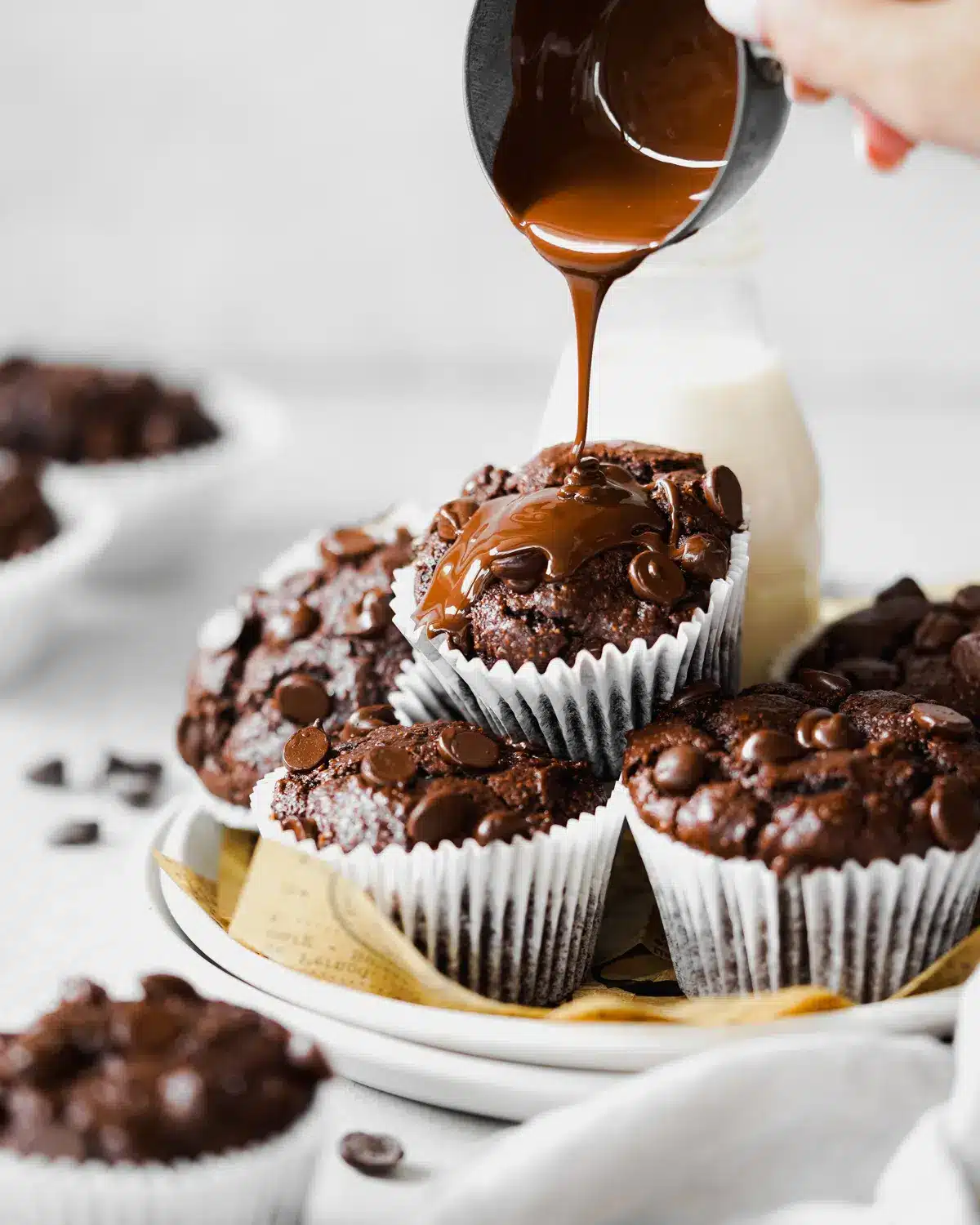 Caramel sauce being poured over vegan chocolate muffins on a white plate.