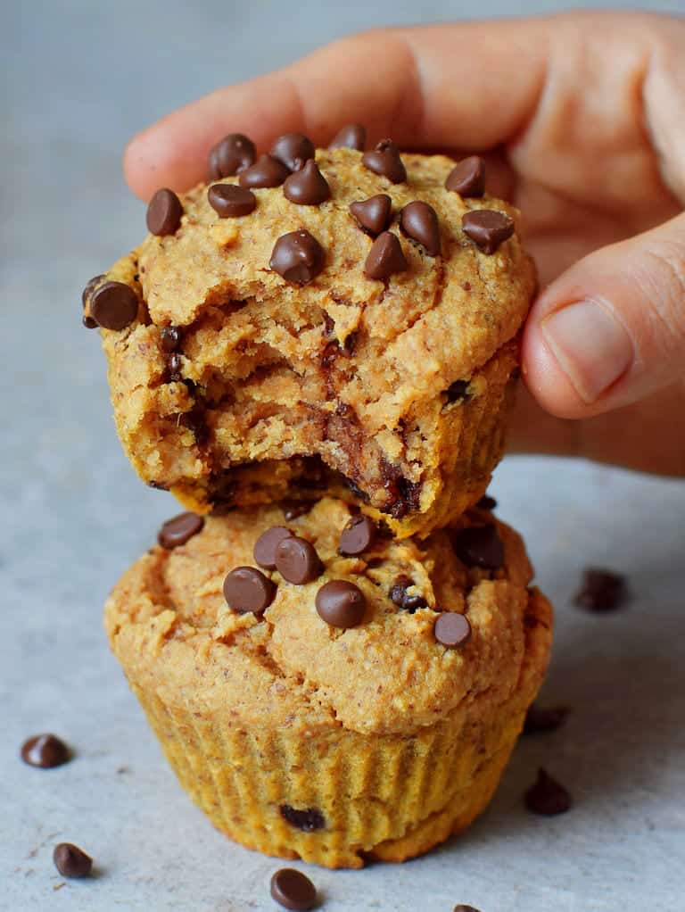 A stack of three vegan chocolate chip muffins with the top one broken in half, showing a fluffy interior studded with chocolate chips.