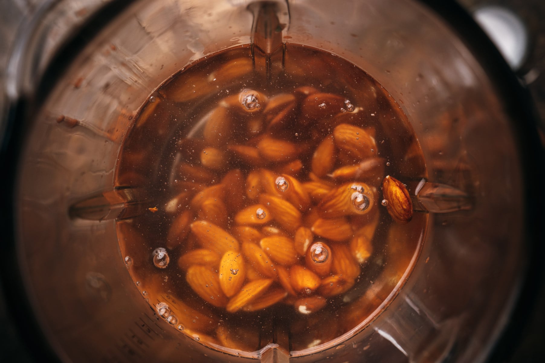 Top view of almonds soaking in water inside a clear bowl, with visible bubbles around the nuts.