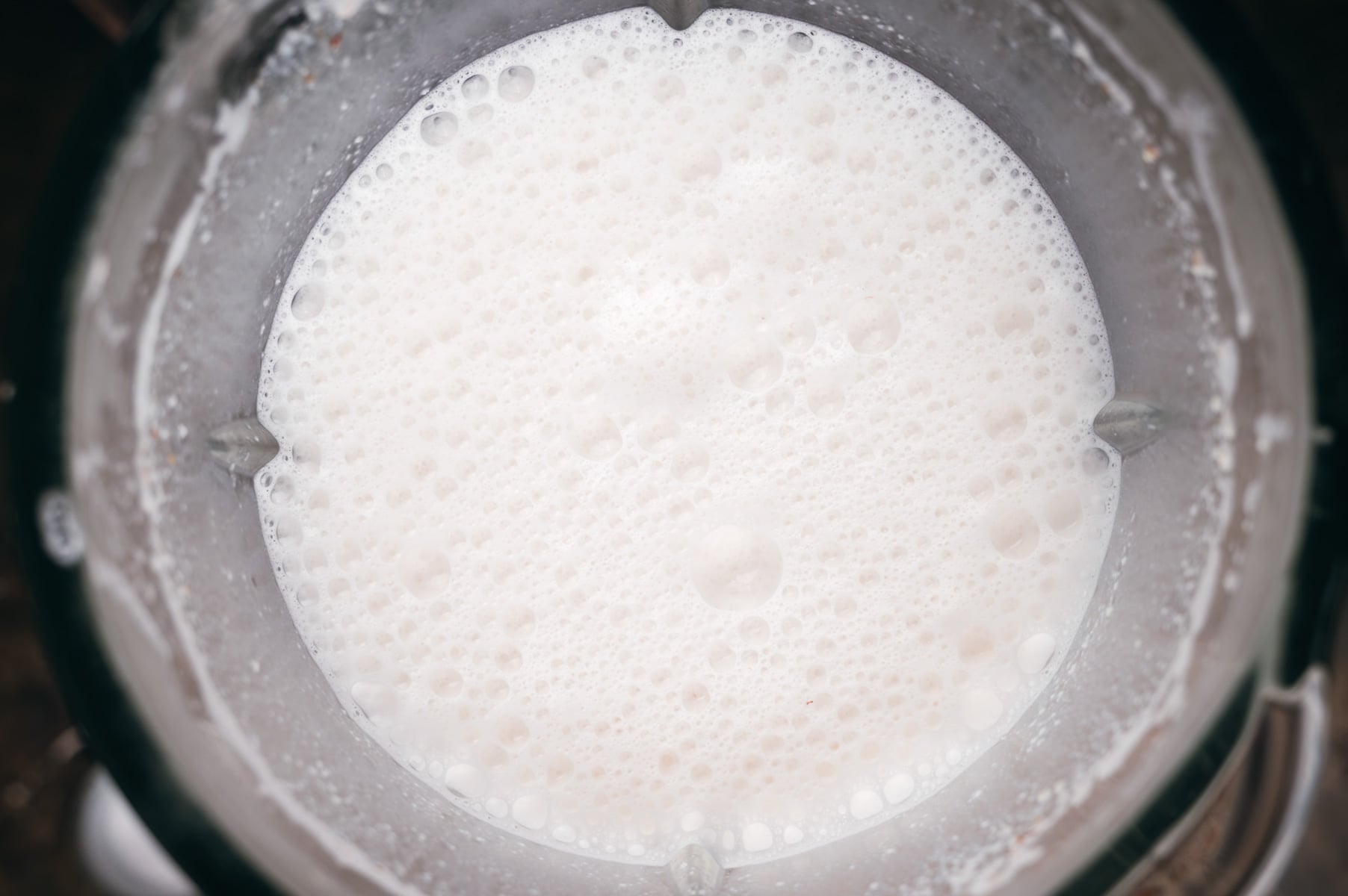 Top view of a glass of milk with foam and bubbles visible on the surface.