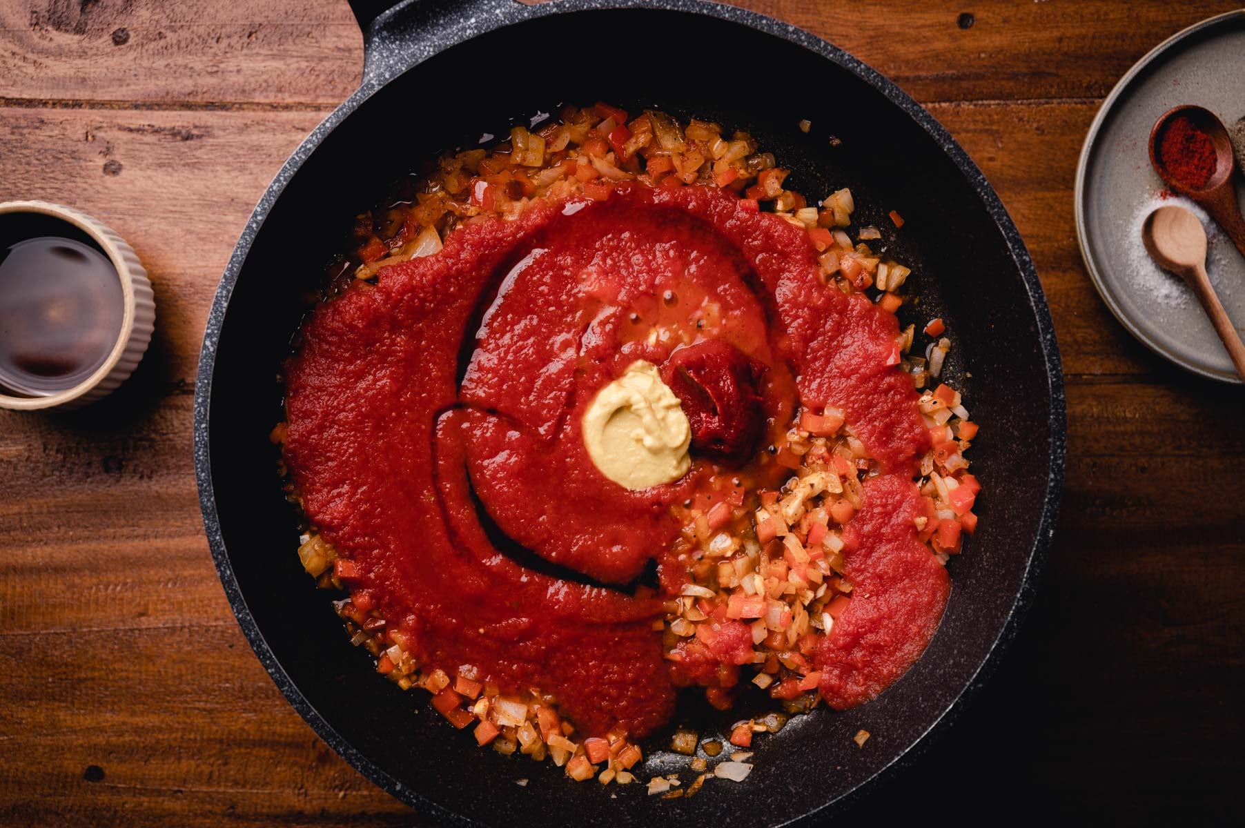 Tomato sauce and a dollop of mustard over sautéed diced vegetables in a cast iron skillet, with spices on the side.
