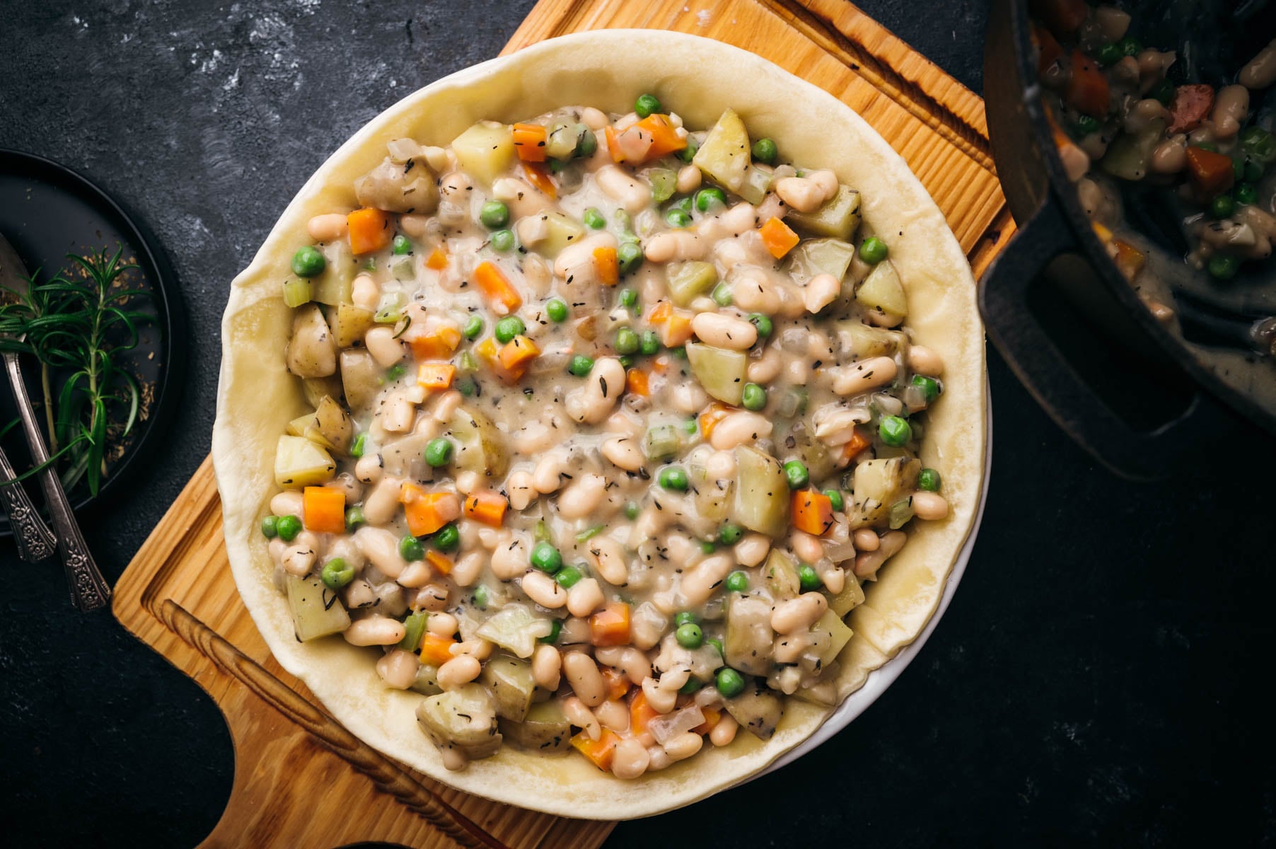 A chicken pot pie with diced vegetables and a creamy sauce, served in a wooden dish on a dark table.