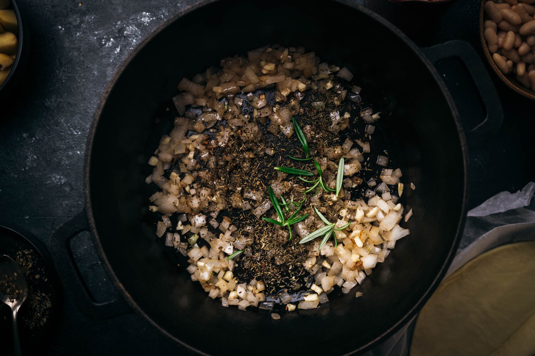 Diced onions and herbs cooking in a black cast iron pot, viewed from above.