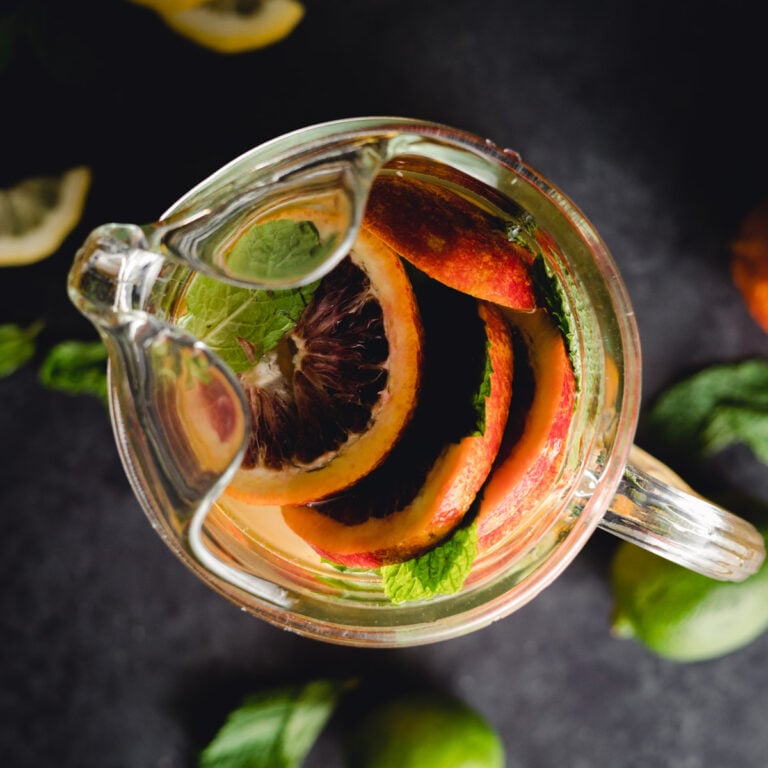 A glass pitcher filled with sliced citrus fruits and mint leaves viewed from above.