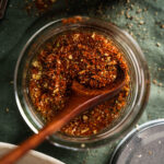 A wooden spoon inside a glass jar filled with a mix of ground spices.