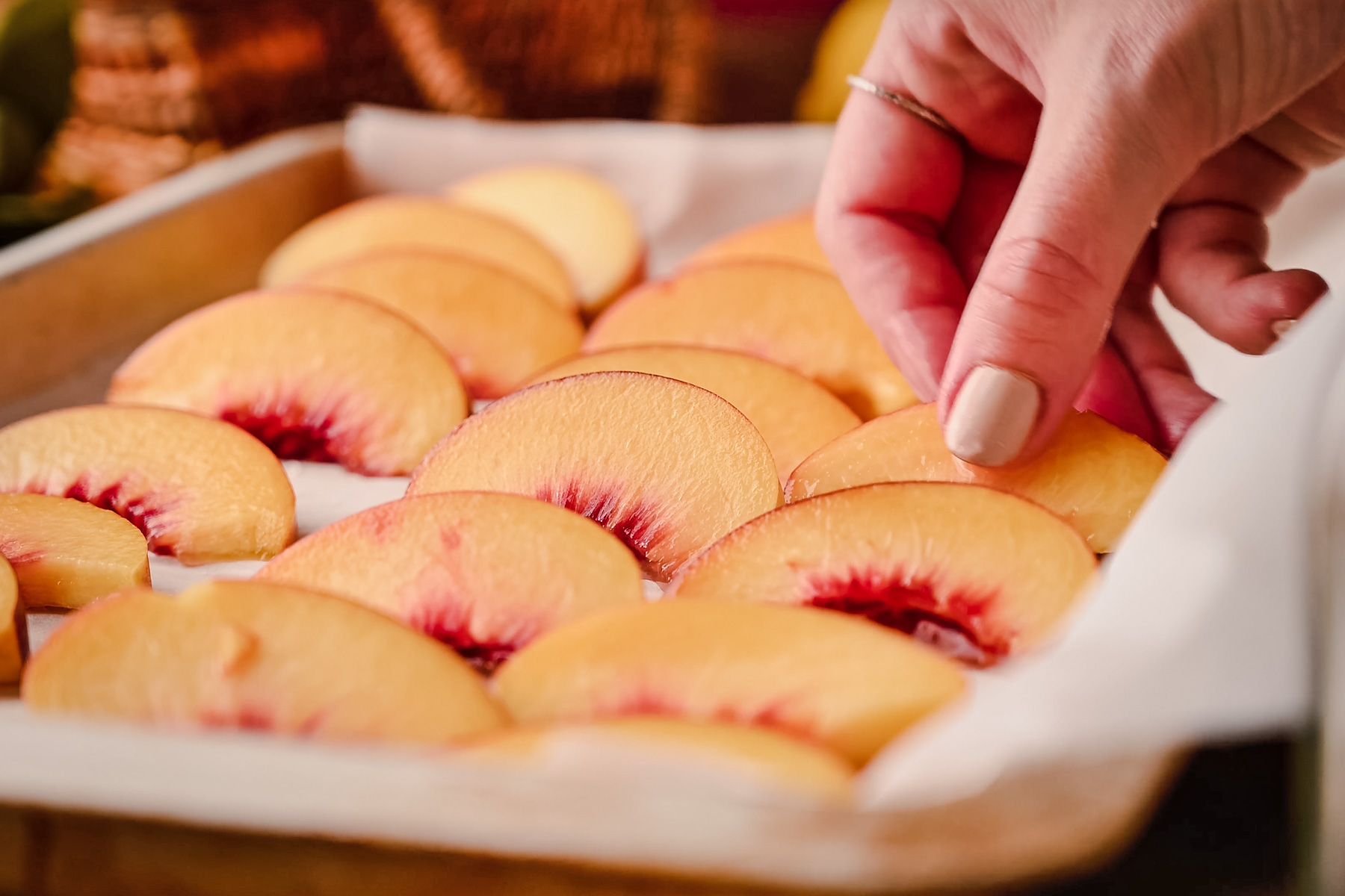 A hand arranges slices of peach on a parchment-lined baking tray.