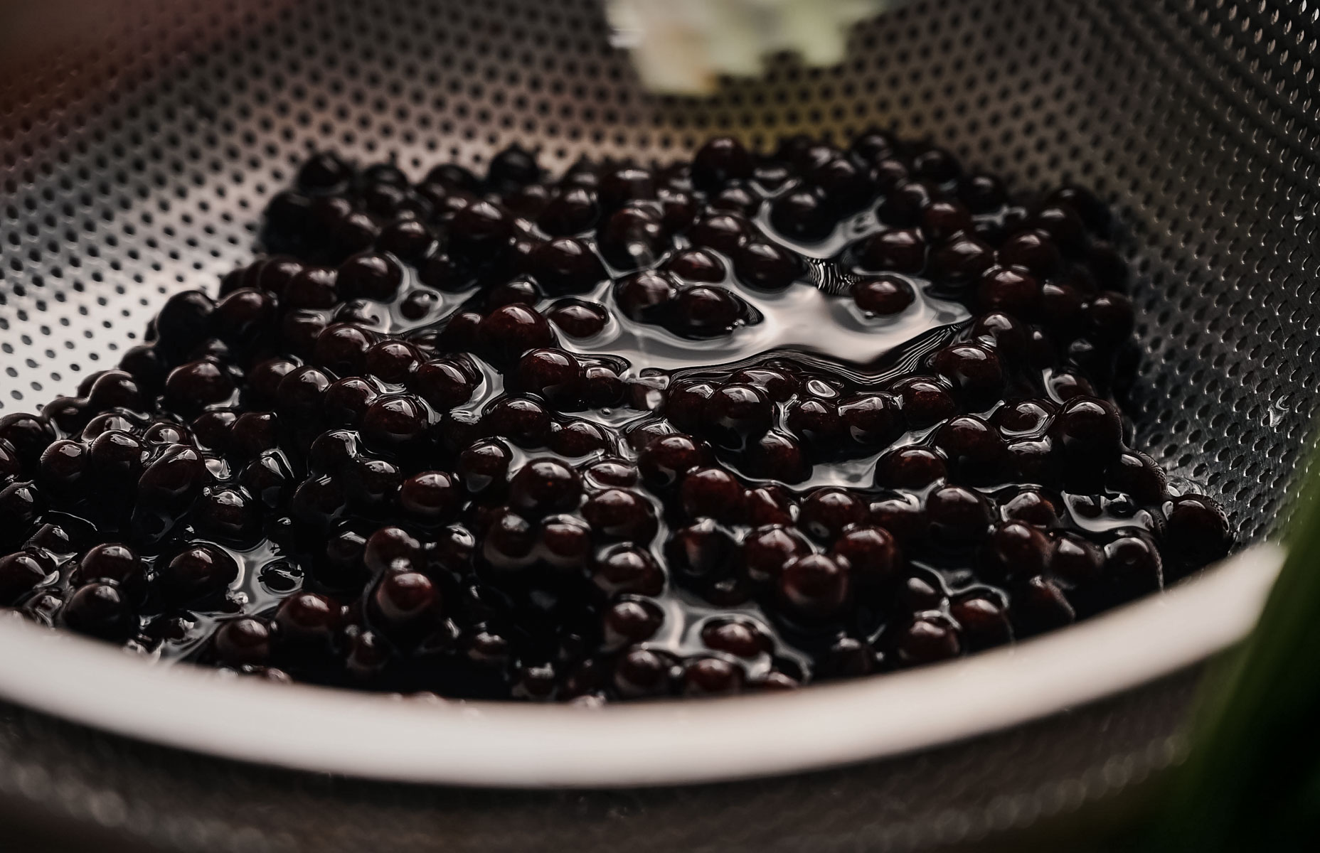 A colander filled with wet, dark tapioca pearls.