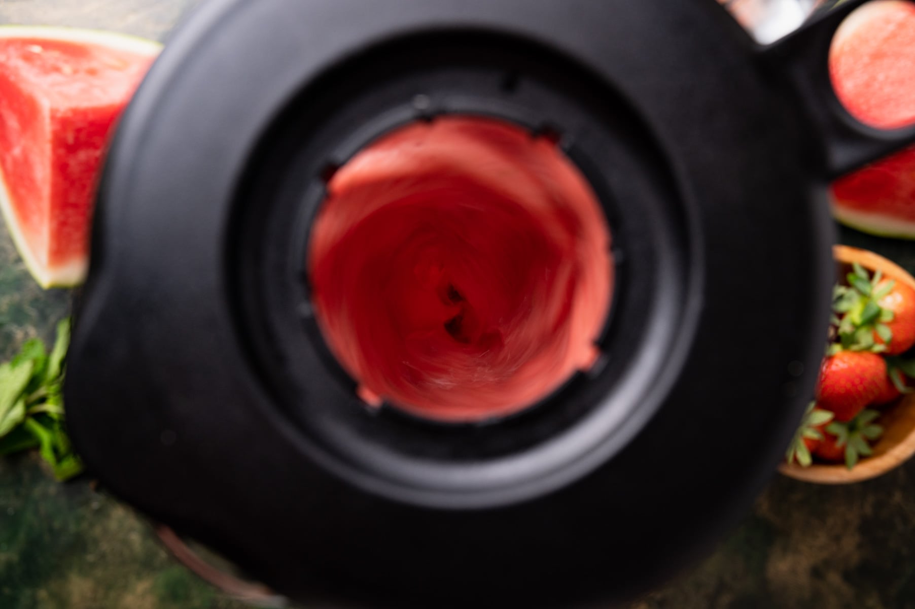 Top-down view of a blender with a pink smoothie being blended, surrounded by watermelon slices and strawberries.
