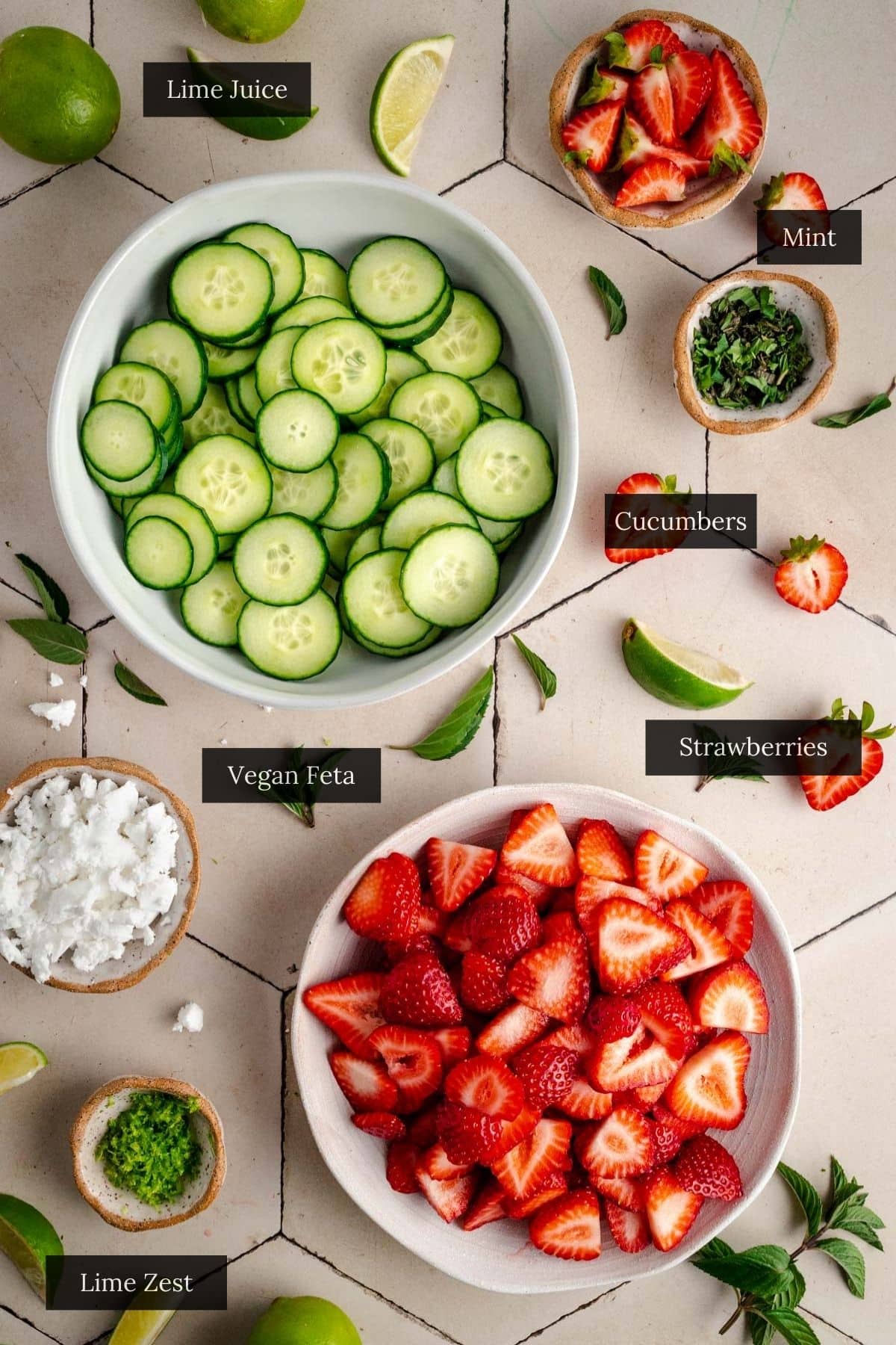 Top-down view of a tiled surface showcasing bowls of sliced cucumbers, strawberries, and more.