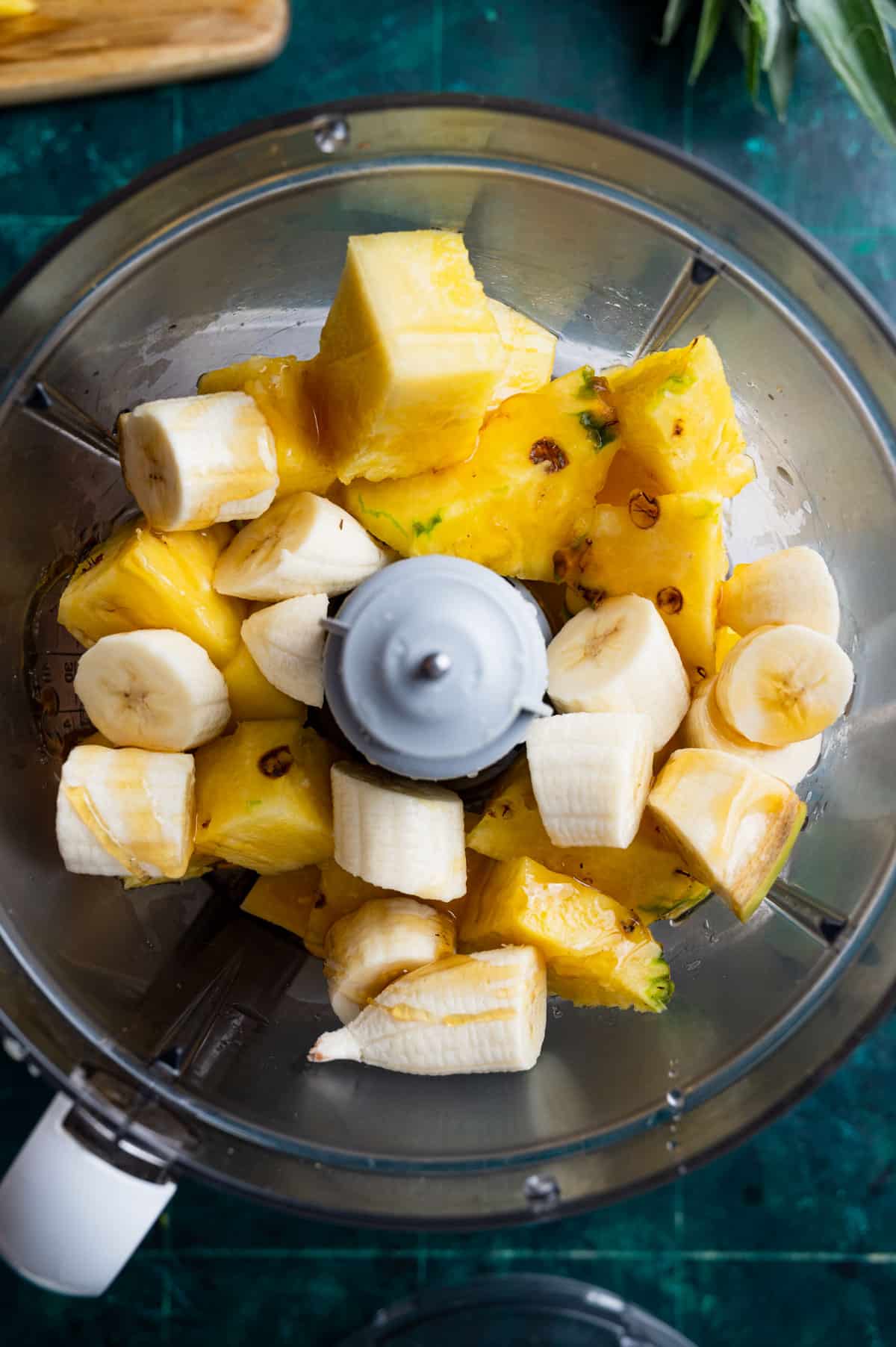A top view of a food processor containing cut pieces of pineapple and banana, ready to be blended.