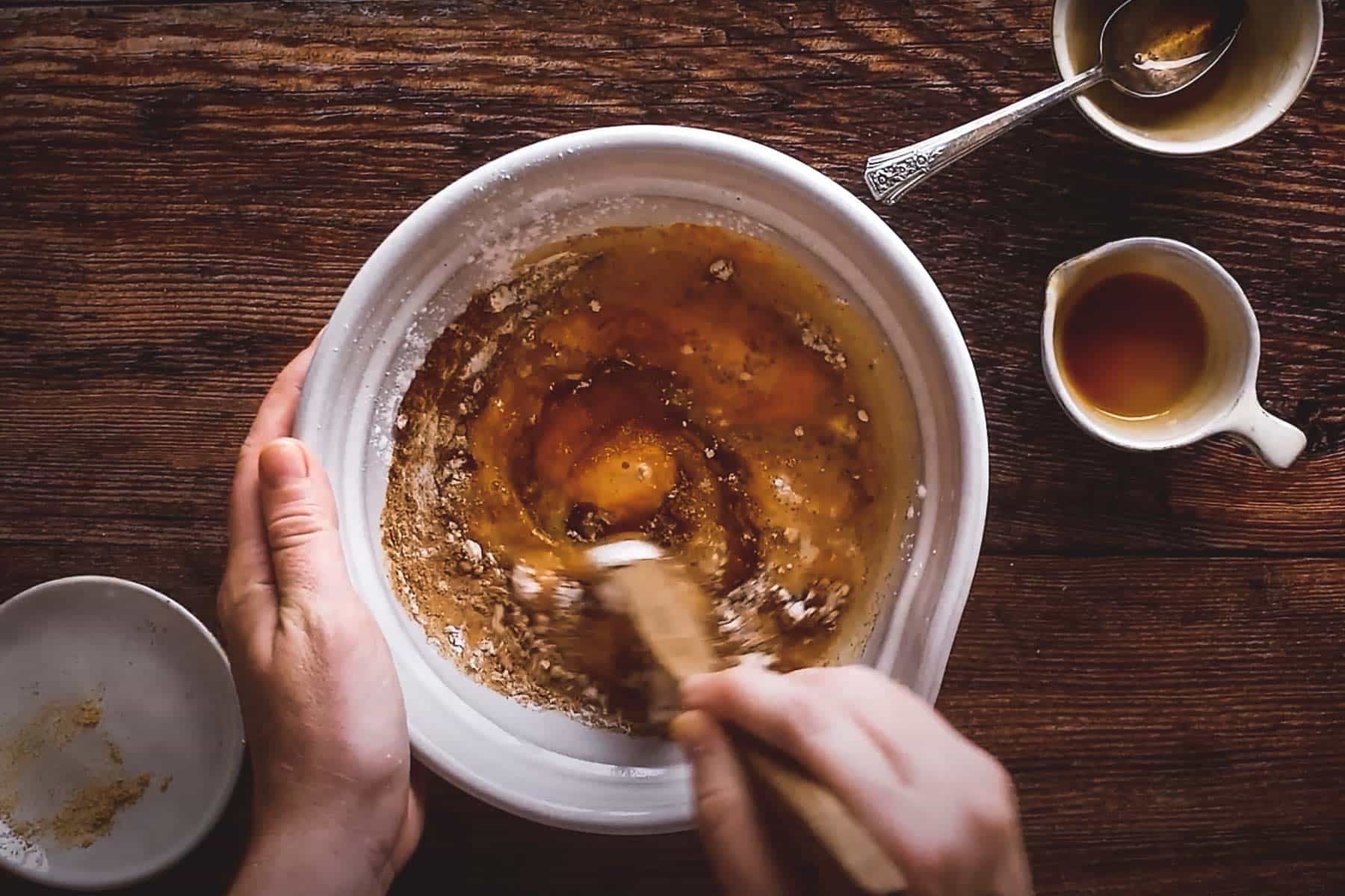 A person is mixing ingredients in a white bowl with a wooden spoon.