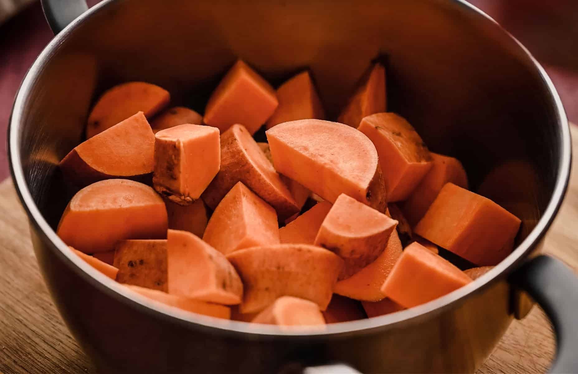 A saucepan filled with chunks of raw sweet potatoes.