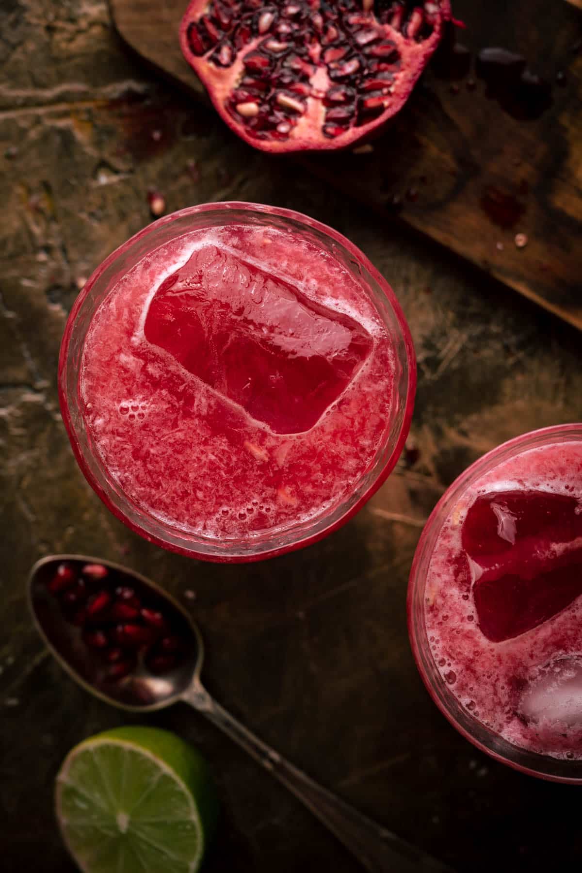 Two glasses filled with pomegranate limeade beside a halved pomegranate.