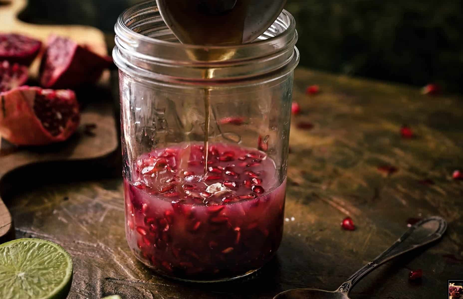Close-up of a glass jar filled with pomegranate seeds and juice, as maple syrup is being poured in.