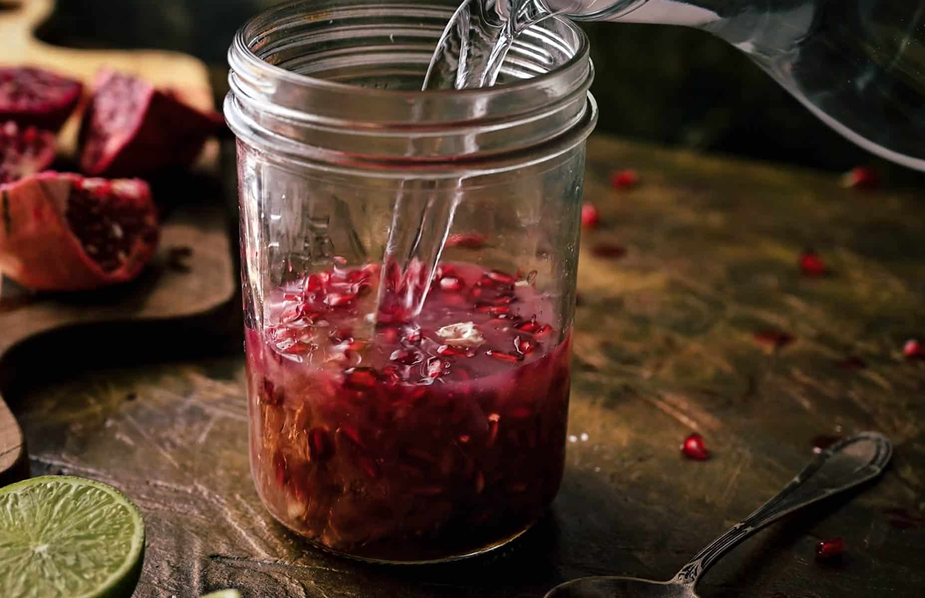 Water is being poured into a mason jar containing pomegranate seeds.