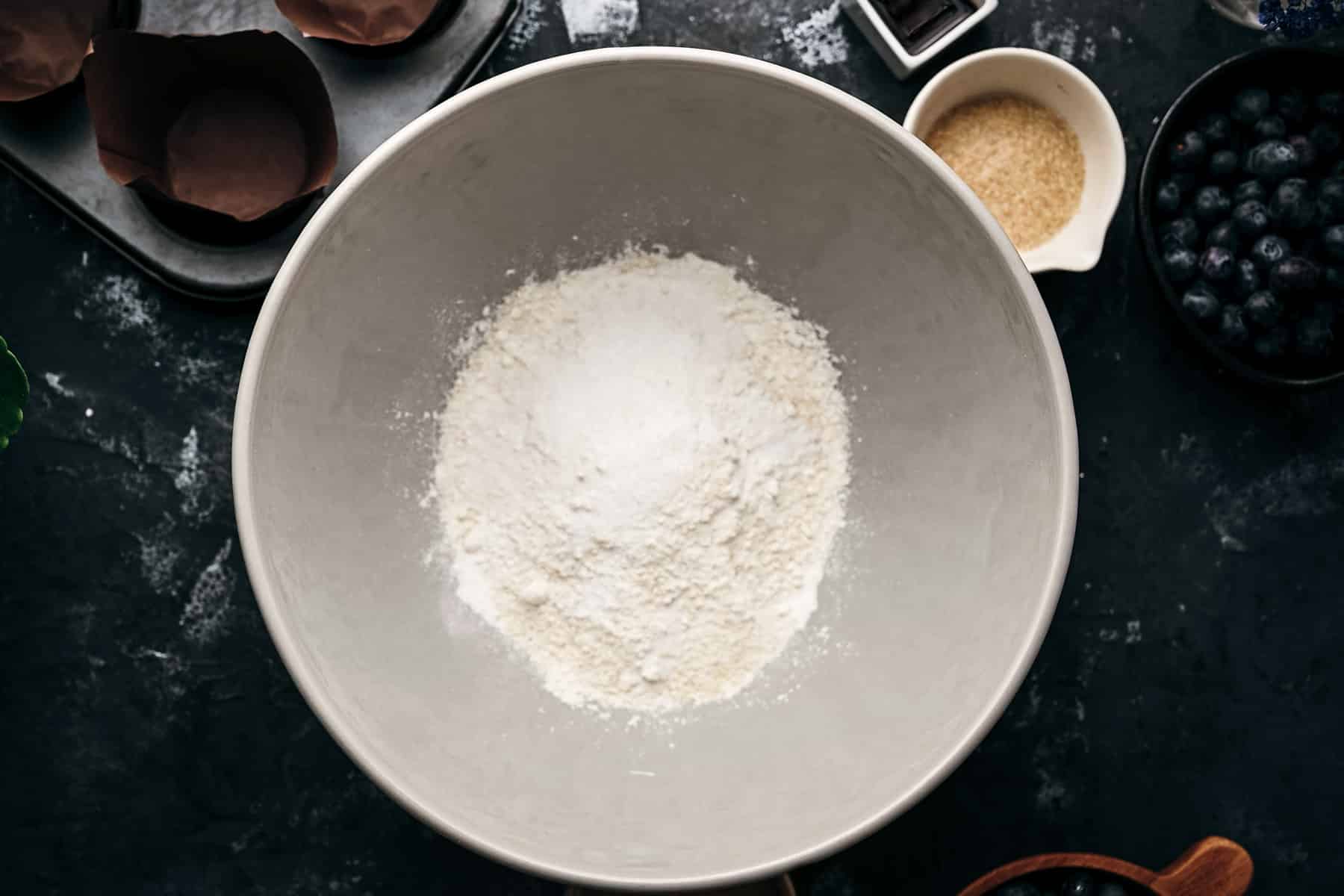A large mixing bowl filled with flour on a dark countertop.