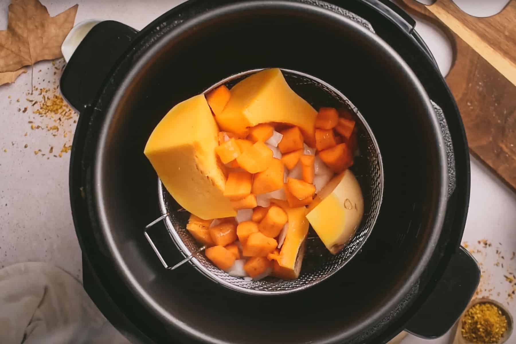 A top view of an Instant Pot containing chopped raw squash and onions placed in a steaming basket.