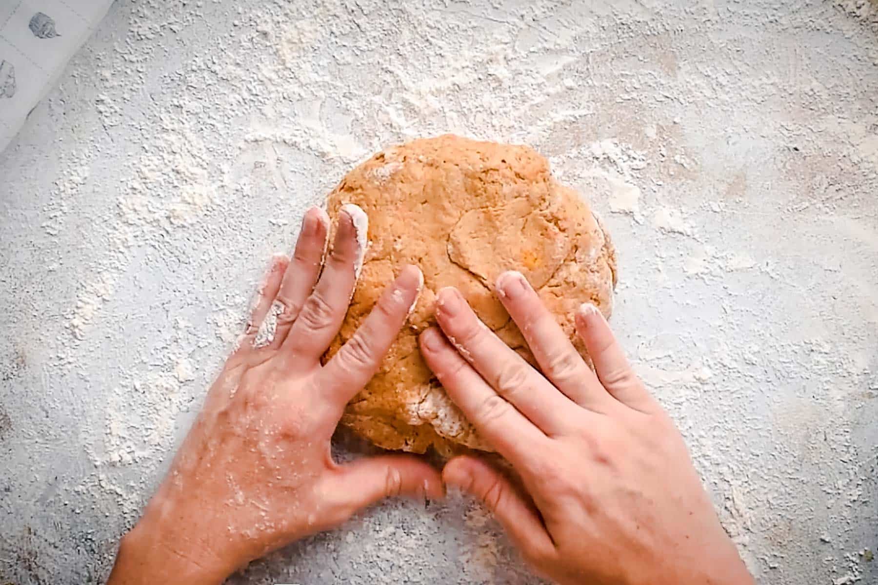 A pair of hands kneads a round mound of dough on a floured surface.