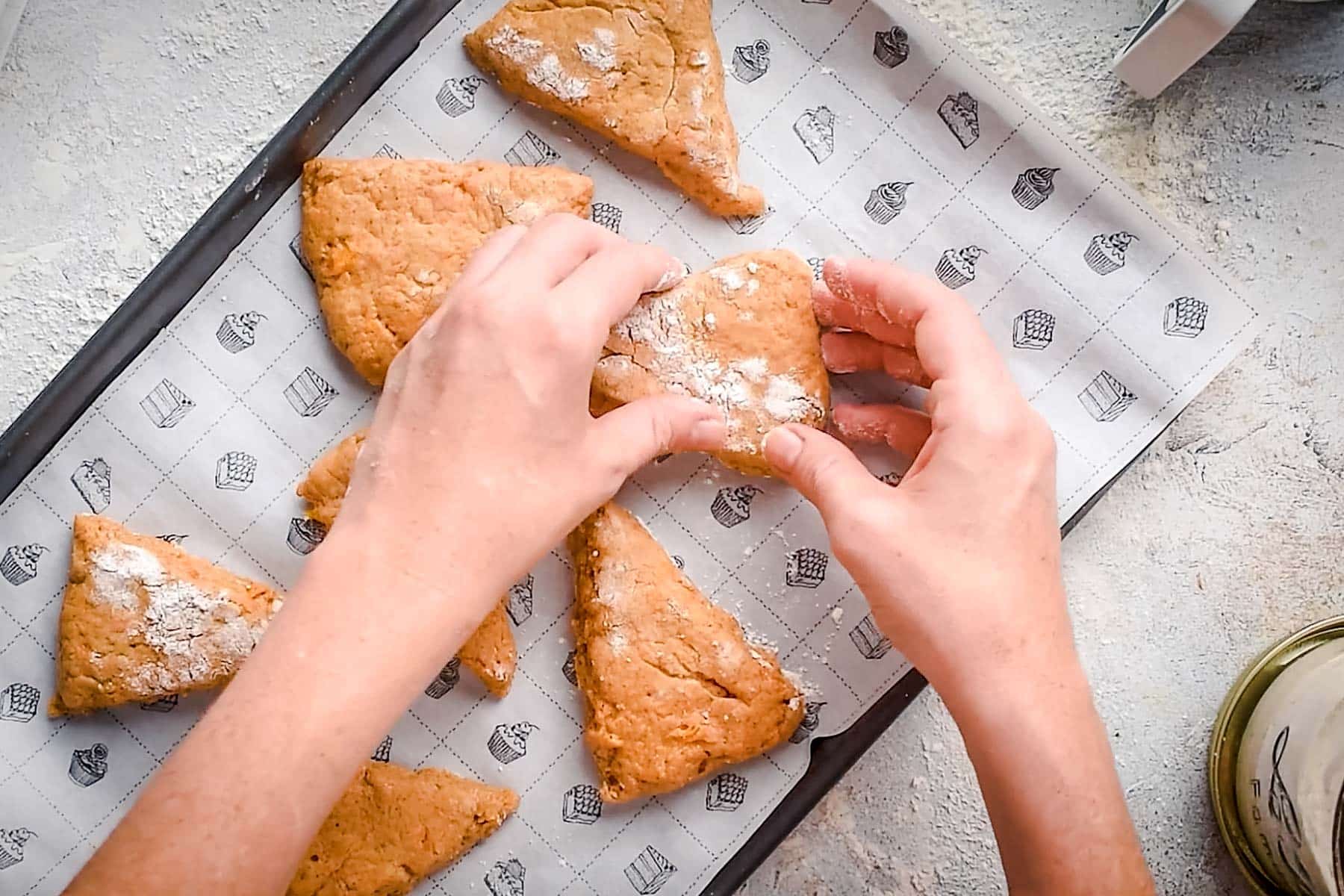 Hands shaping triangular pieces of dough on a baking sheet lined with parchment paper.