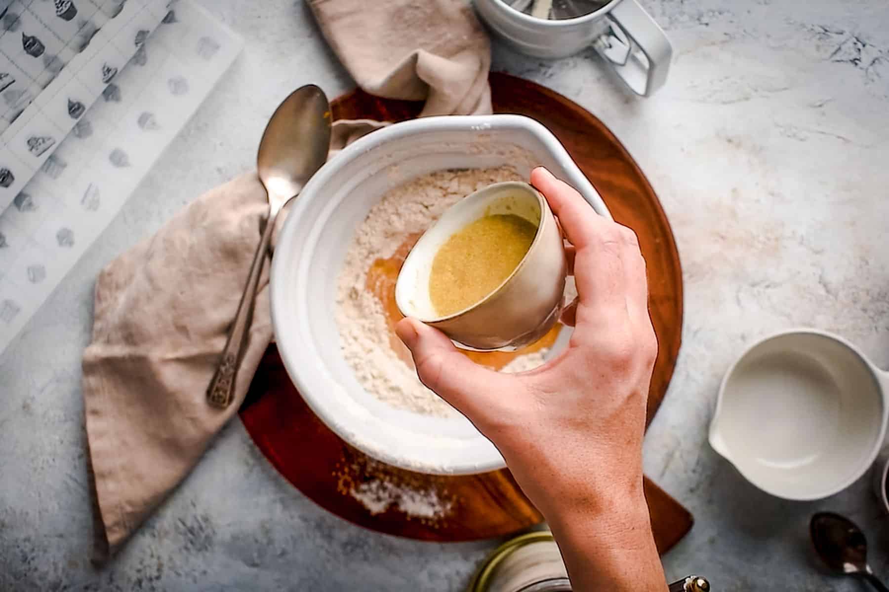 A hand holding a small small bowl of flax egg over a mixing bowl that contains flour.