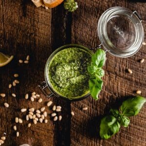 A jar of vibrant pesto with a basil garnish on a wooden table.