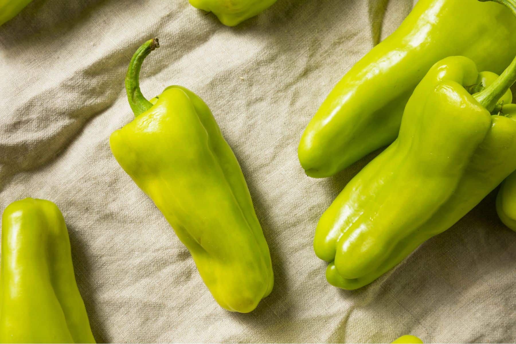 Several bright green peppers on a textured light fabric surface.