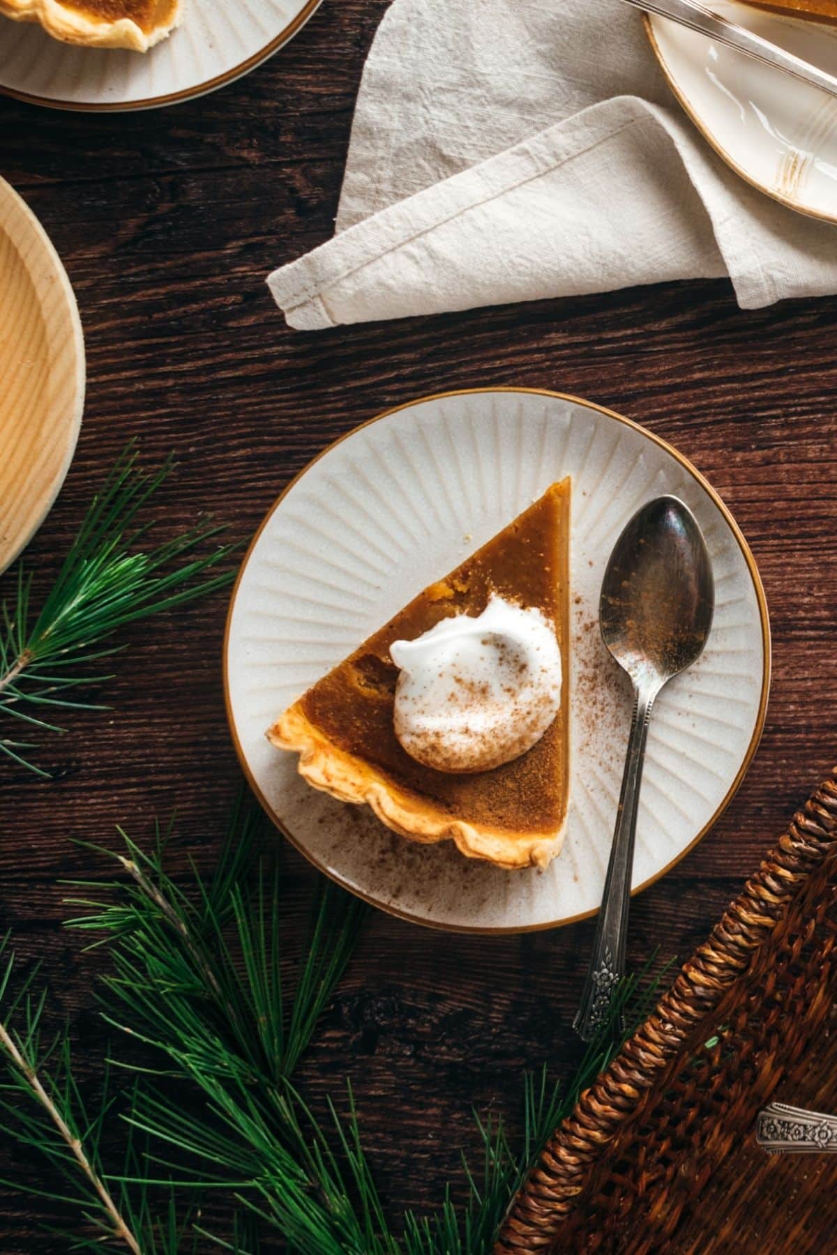 A slice of pumpkin pie with whipped cream on a plate, alongside a spoon.