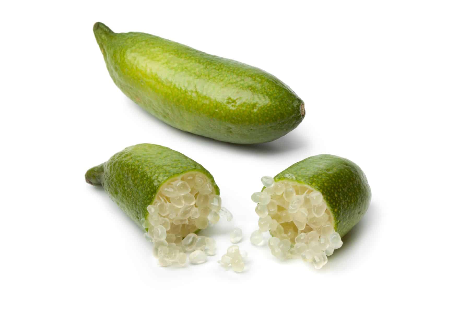 Two whole green finger limes, one cut open to reveal pearl-like citrus vesicles inside.