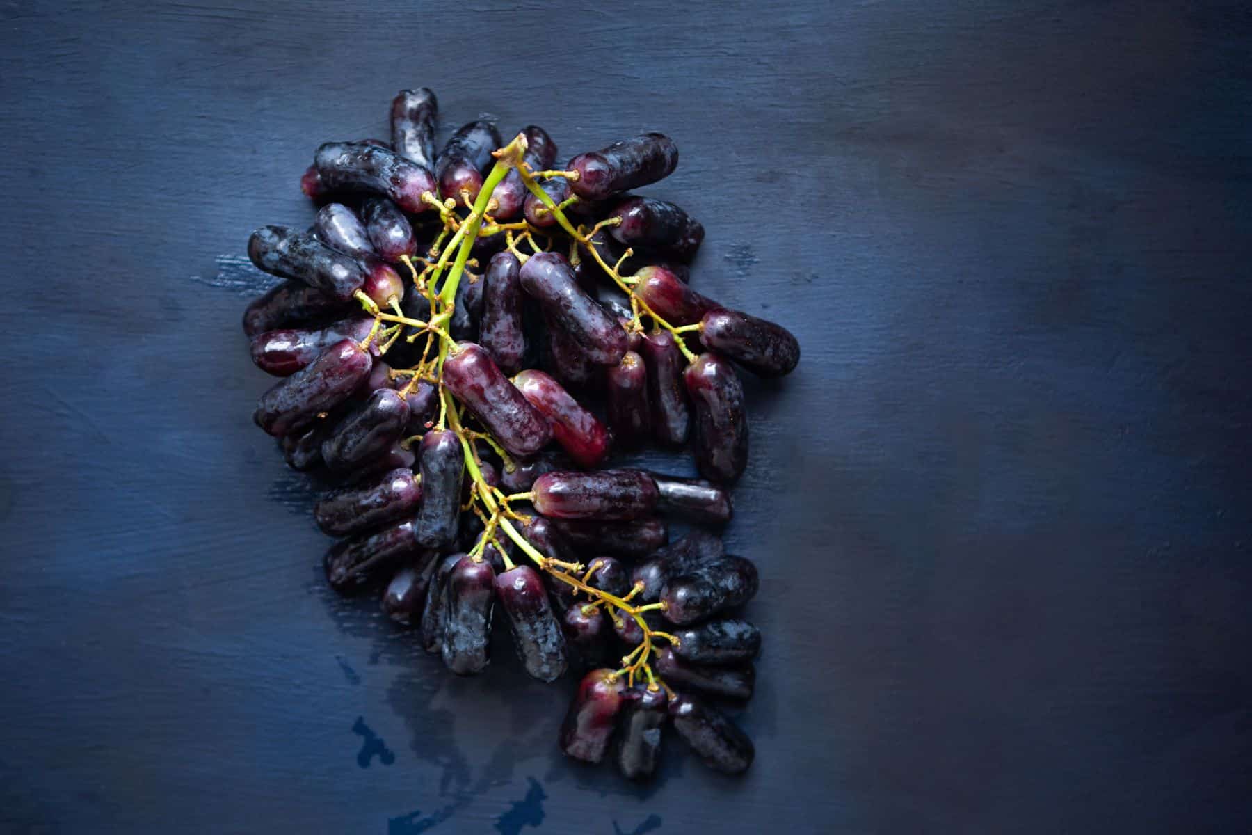A cluster of dark purple grapes with elongated shapes on a dark blue background.