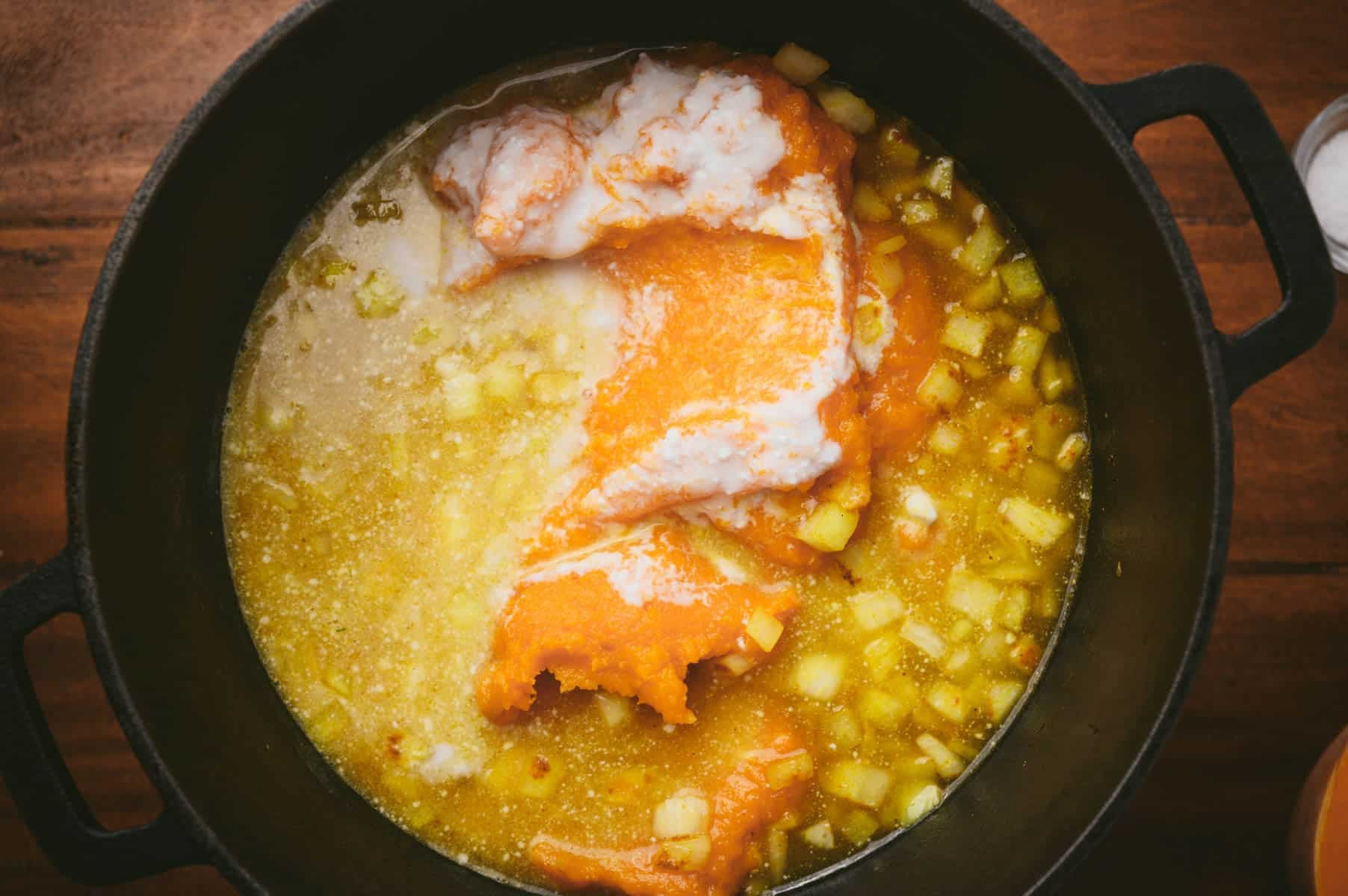 Ingredients being cooked in a black pot including onion, broth, pumpkin, and coconut milk.