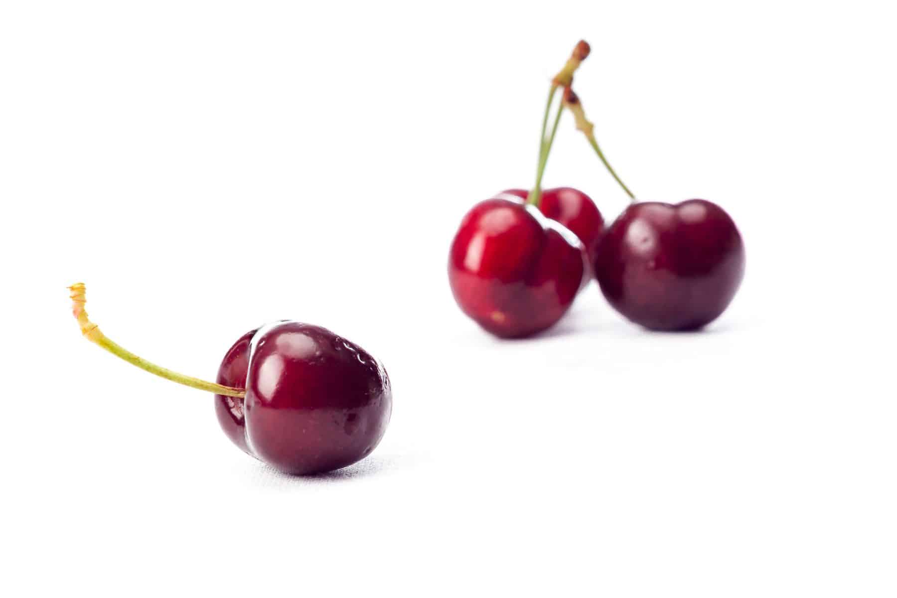 Three red cherries on a white background, with one cherry in the foreground and two in the background.