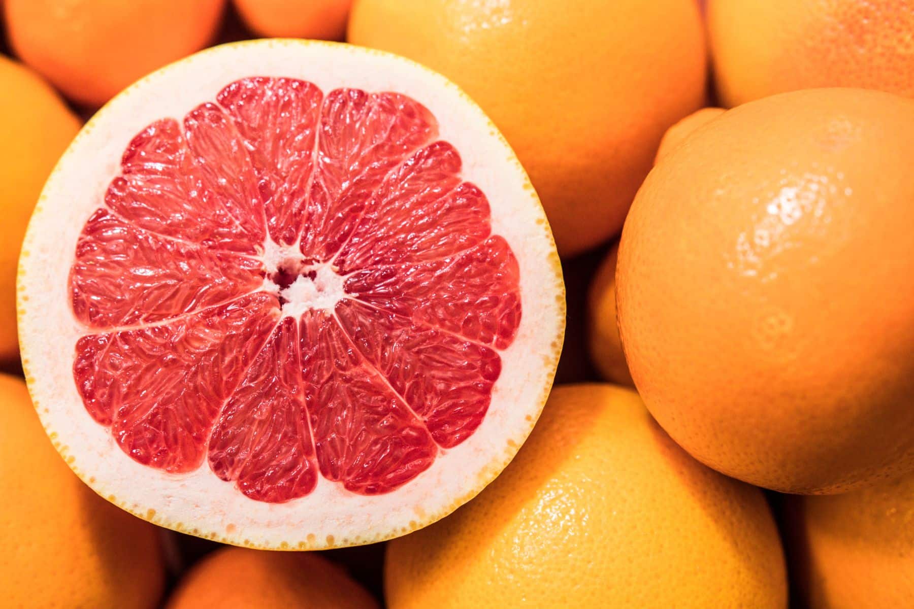 A close-up of a halved grapefruit showing its pink interior, surrounded by whole grapefruits.