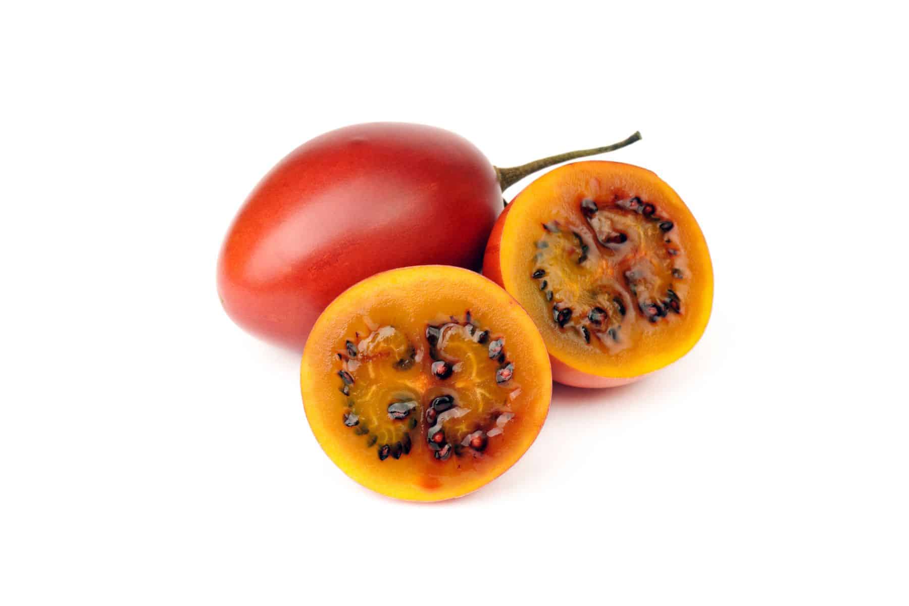 Two tamarillos, one whole and one halved, showing their red skin and fleshy orange interior with dark seeds, on a white background.