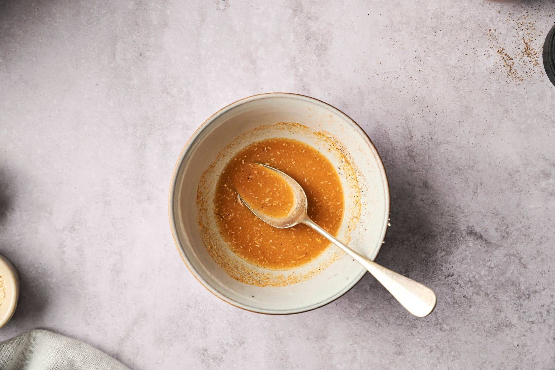 A bowl with a spices and liquid mixture with a spoon inside.